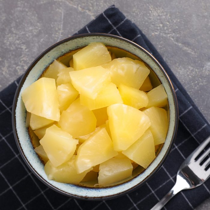 Yummy canned pineapple in bowl on grey table, flat ordinary