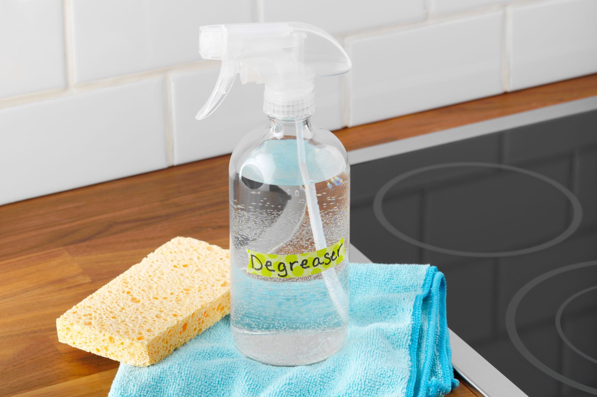 Homemade degreaser Cleaner in a spray bottle with a sponge and microfiber cloth on a kitchen counter near a stovetop