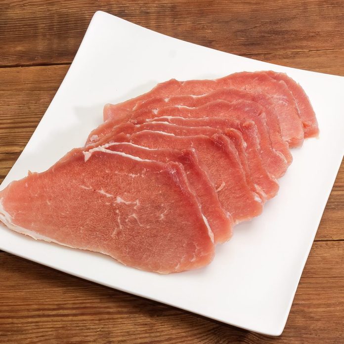 Uncooked defrosted pork slices on a square dish