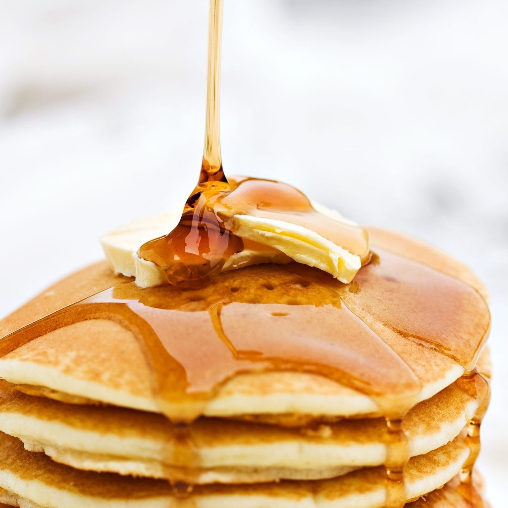 Maple syrup pouring onto pancakes. Shallow DOF with focus on syrup and butter.