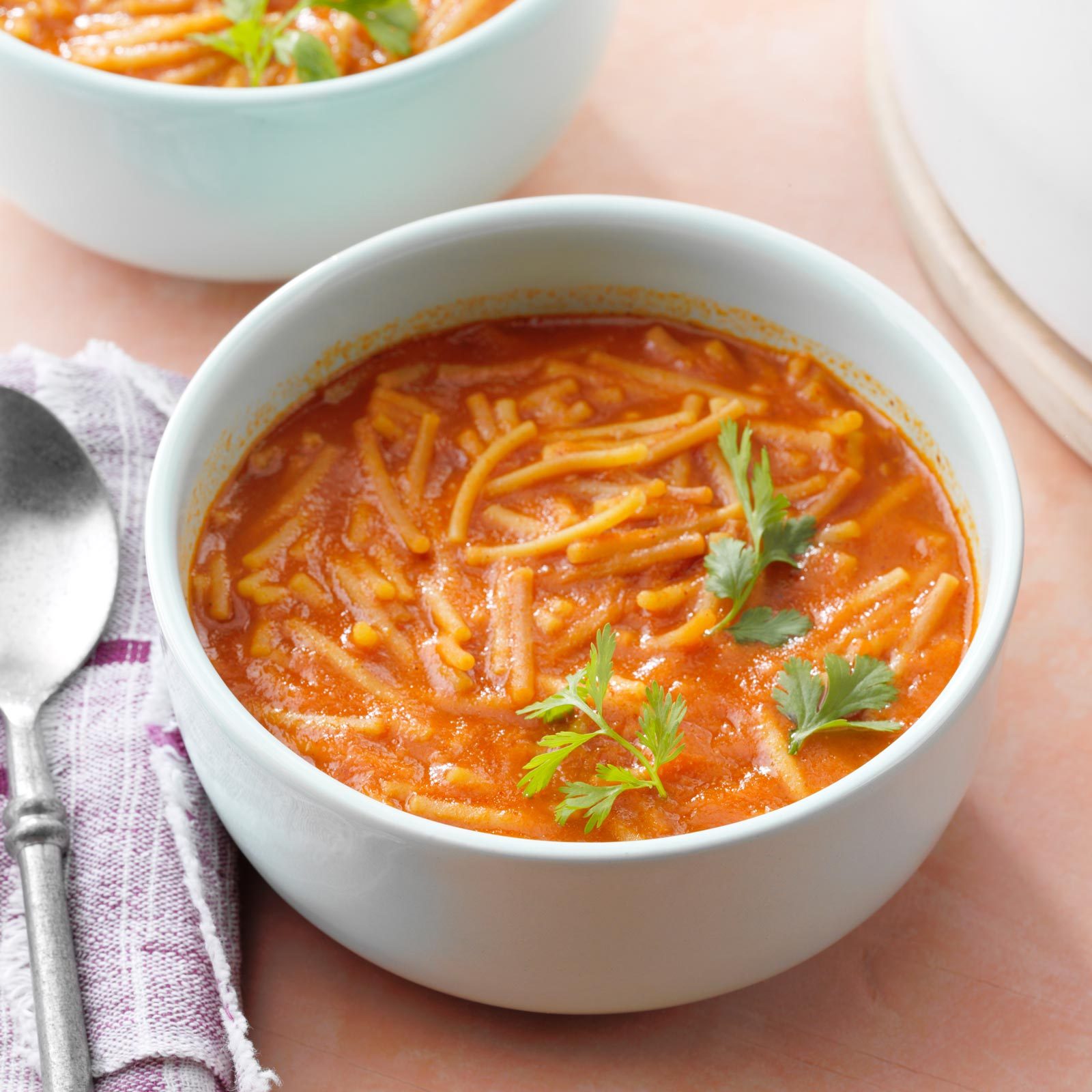 white bowl of Sopa De Fideo with a cloth napkin and spoon