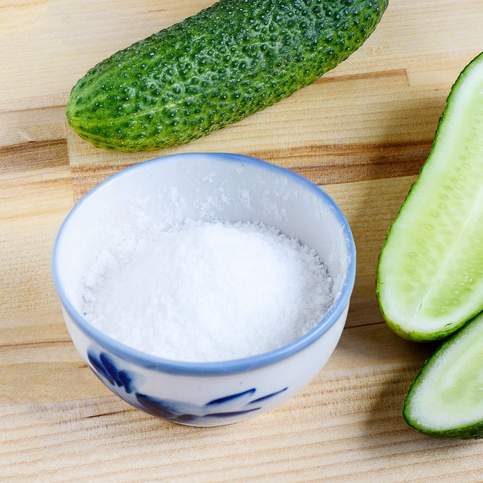 Pickle Salt in a small bowl next to cucumbers on a wooden surface