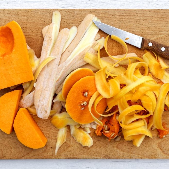 Cut up butternut squash with peels and knife on brown wood chopping board isolated on white from above.