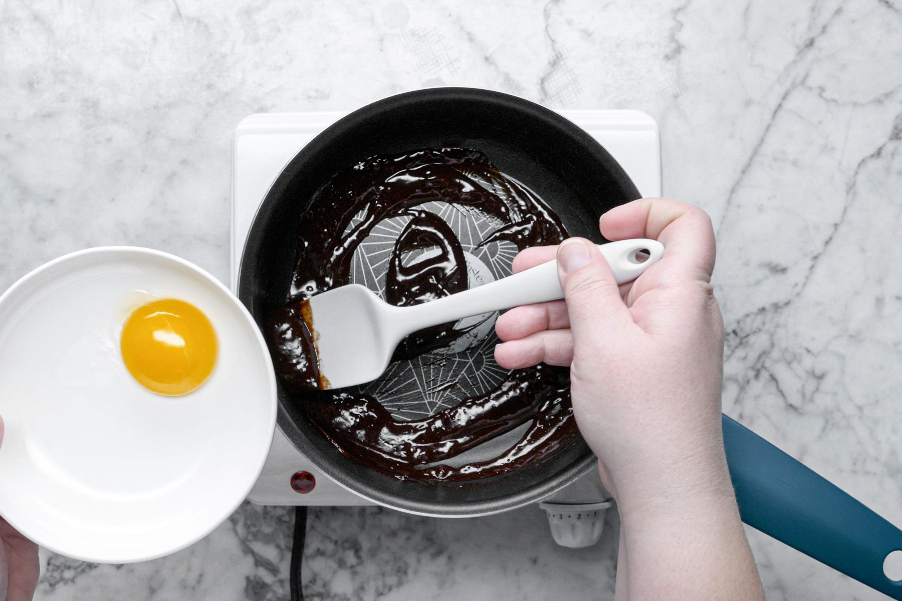 Melting the chocolate in a large pan while holding egg yolk in a plate