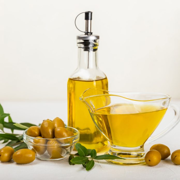 Olive oil in a bottle and gravy boat on the kitchen table. Oil bottle with branches and fruits of olives