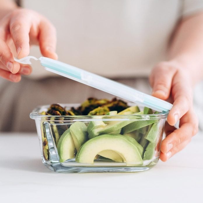 woman putting lid on a storage container filled with sliced avocado