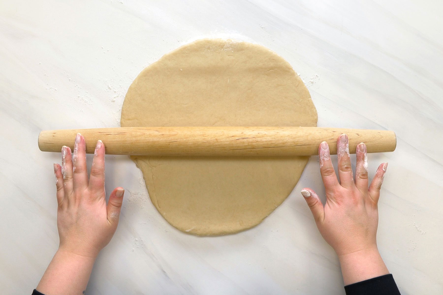 A person rolling the dough on a marble surface