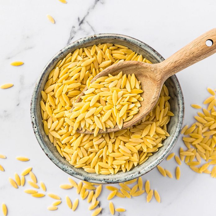 Raw Orzo Pasta (Risoni) In Bowl With Wooden Spoon On Marble Background