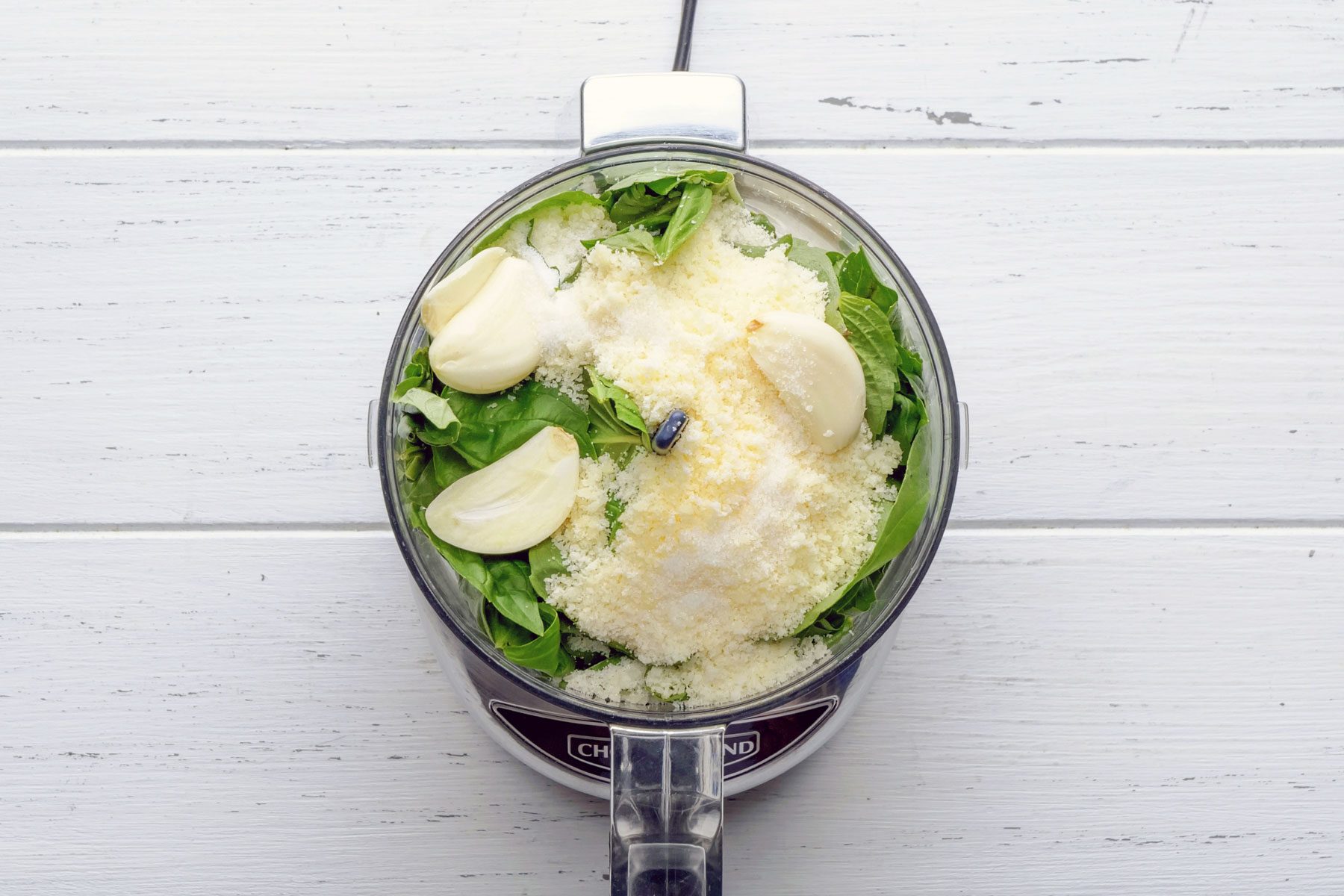 grated cheese, garlic and Basil leaves in a blender on a wooden table