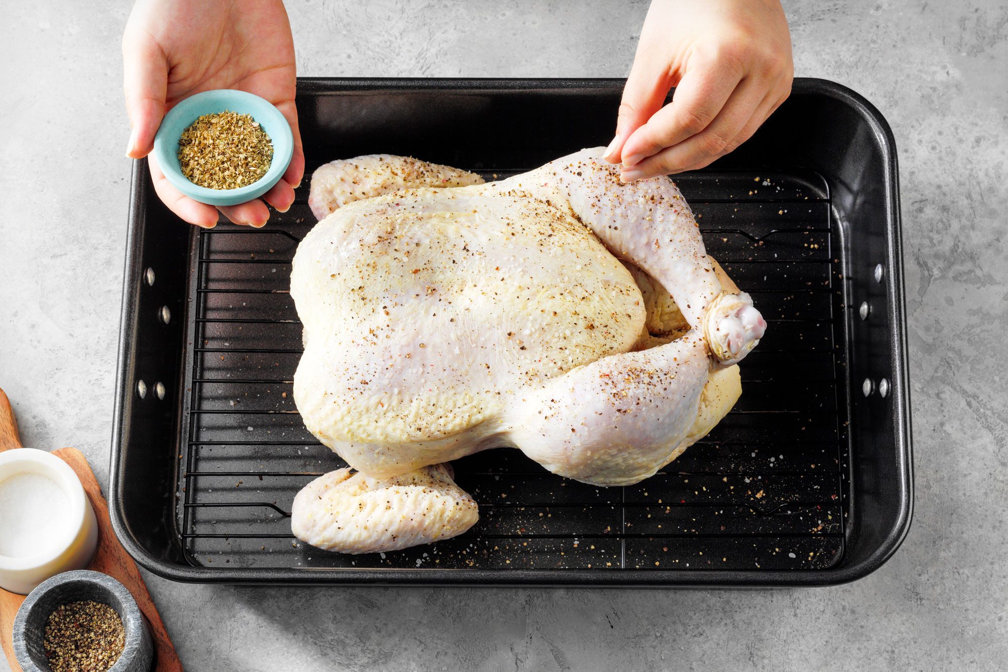 Sprinkling Oregano over chicken placed in a roasting pan on marble surface
