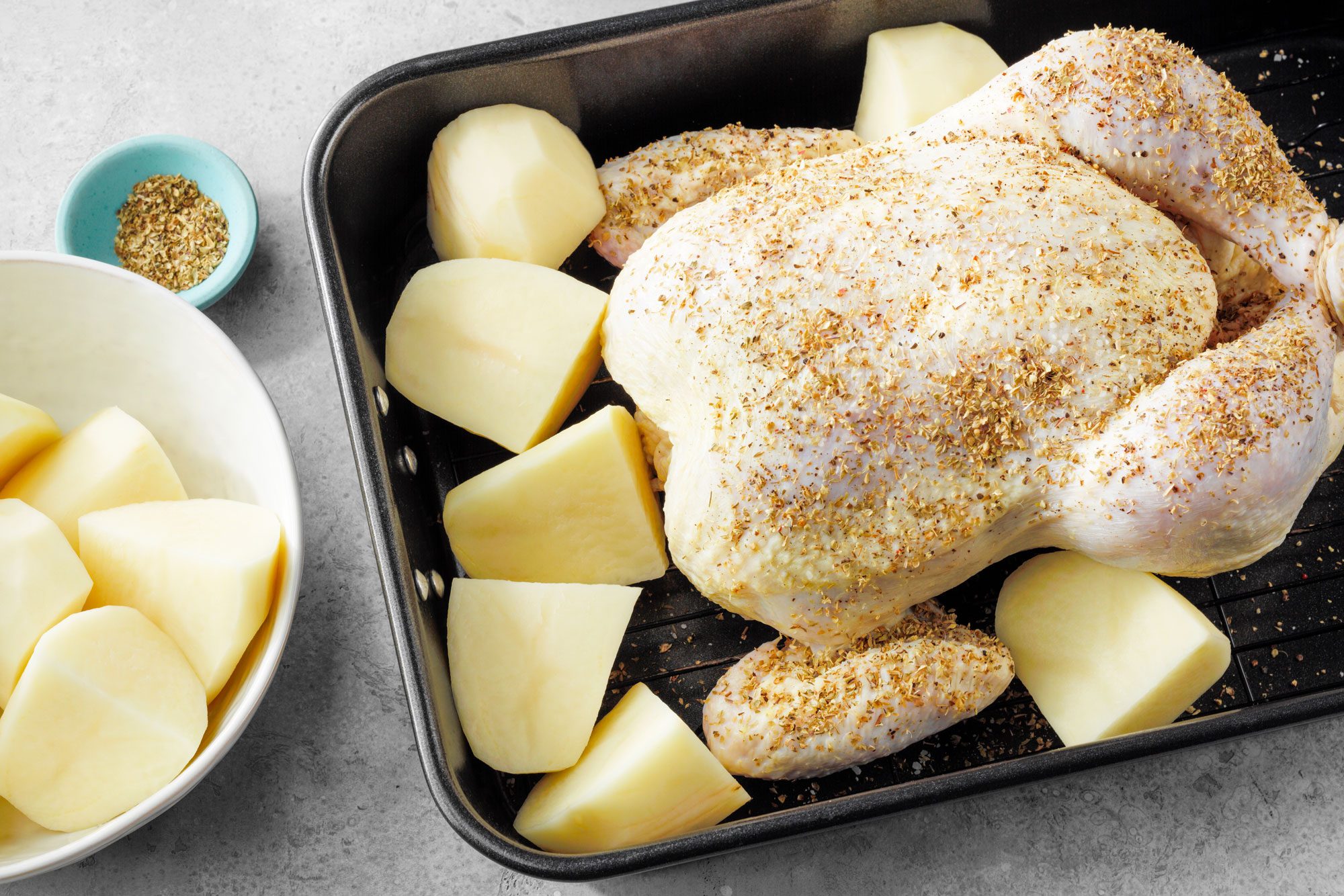 Seasoned Chicken And Potatoes placed in a roasting pan on marble surface