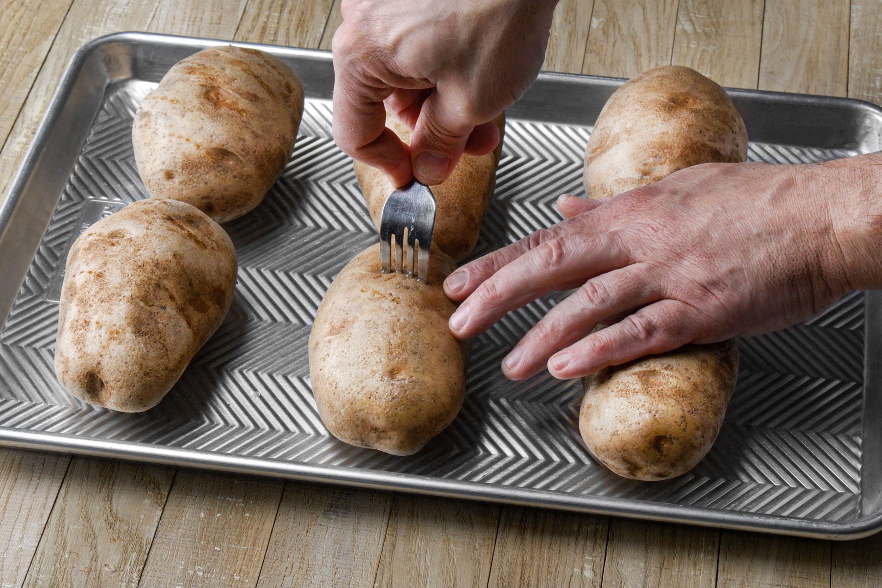 Piercing potatoes using a fork on a baking dish 