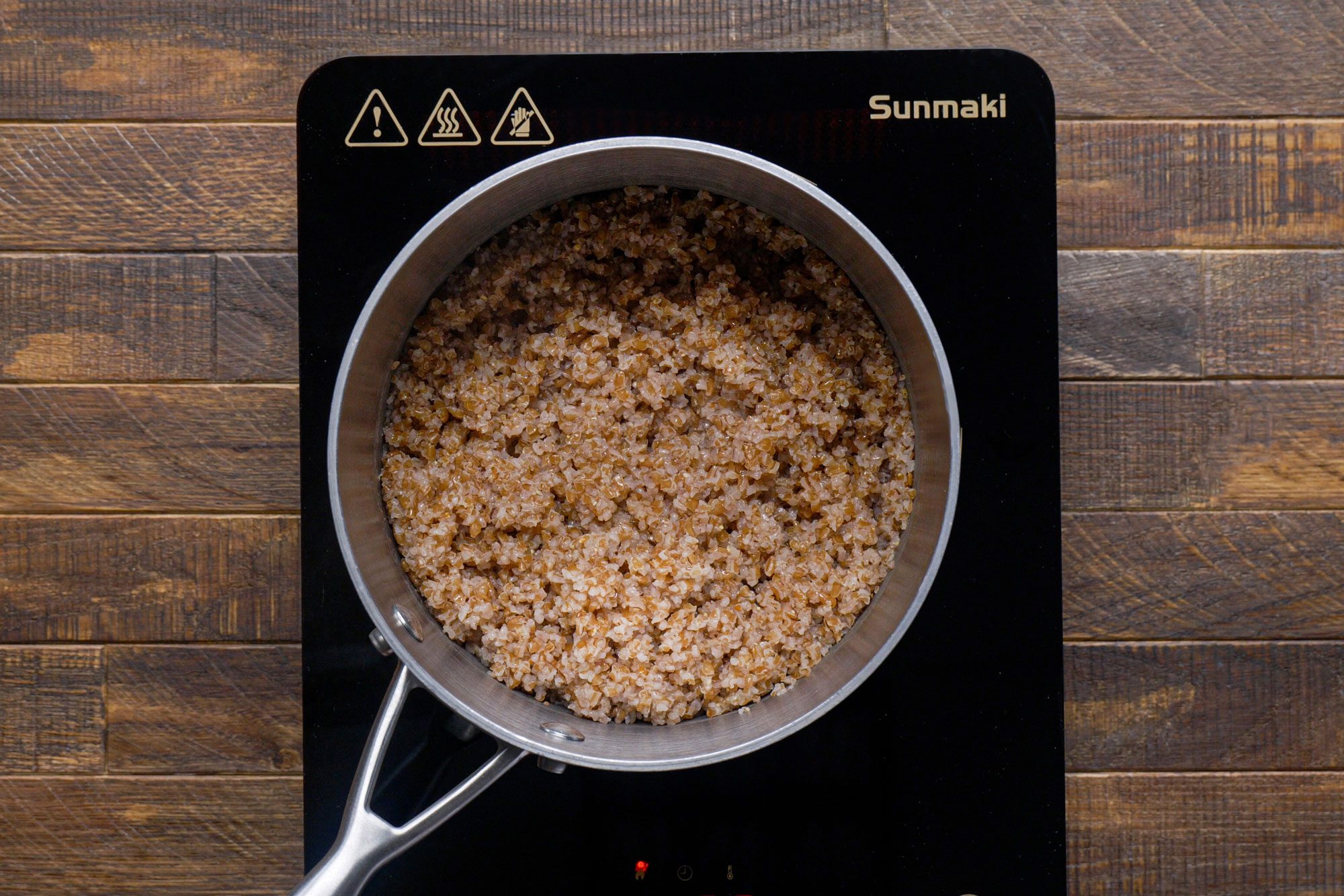 overhead shot of bulgur in a saucepan on a induction cooktop on wooden surface