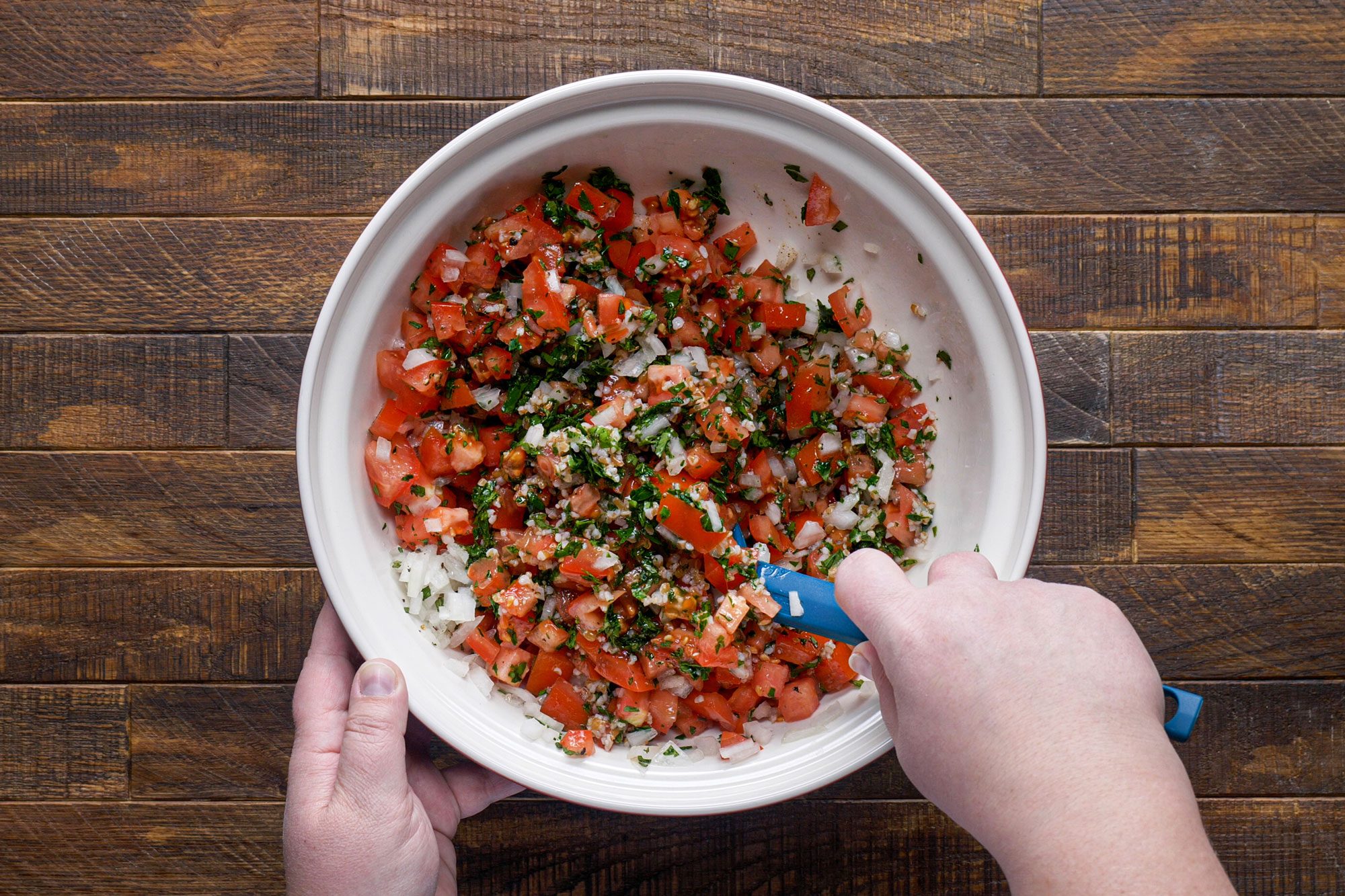 overhead shot of mixing tabbouleh in a large bowl on wooden surface