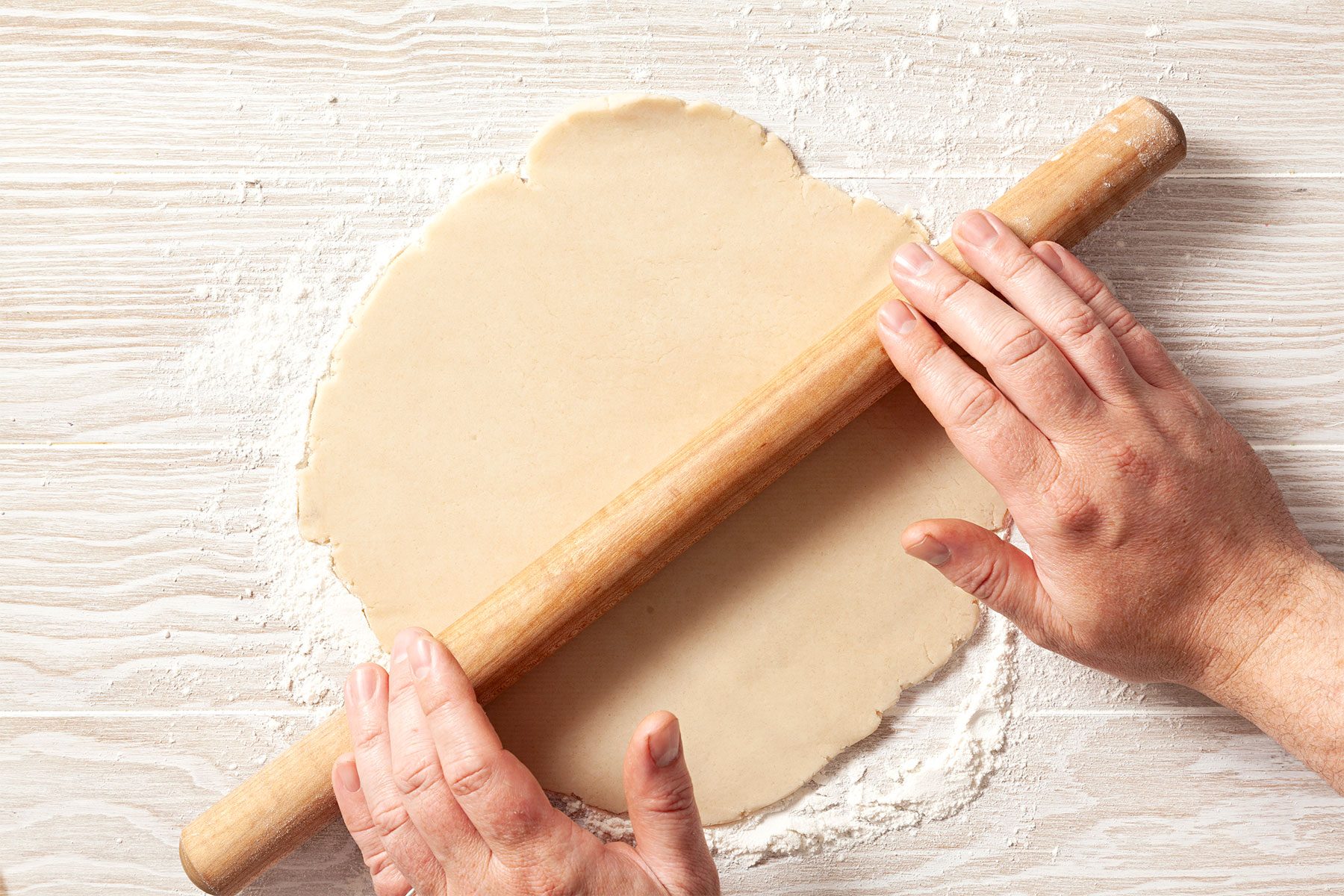 overhead shot; wooden background; On a lightly floured surface, rolling dough into thick circle;