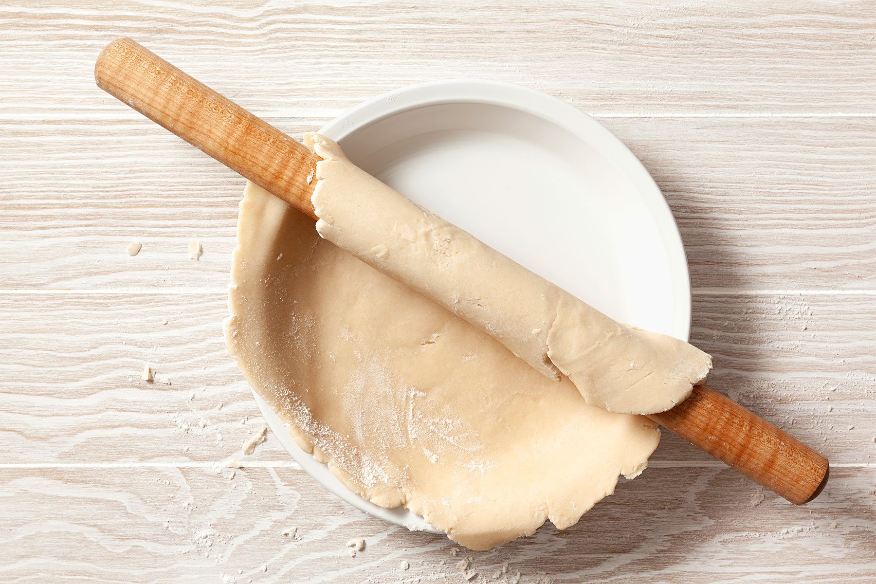 overhead shot; wooden background; rolling dough circle on roller over pie plate;