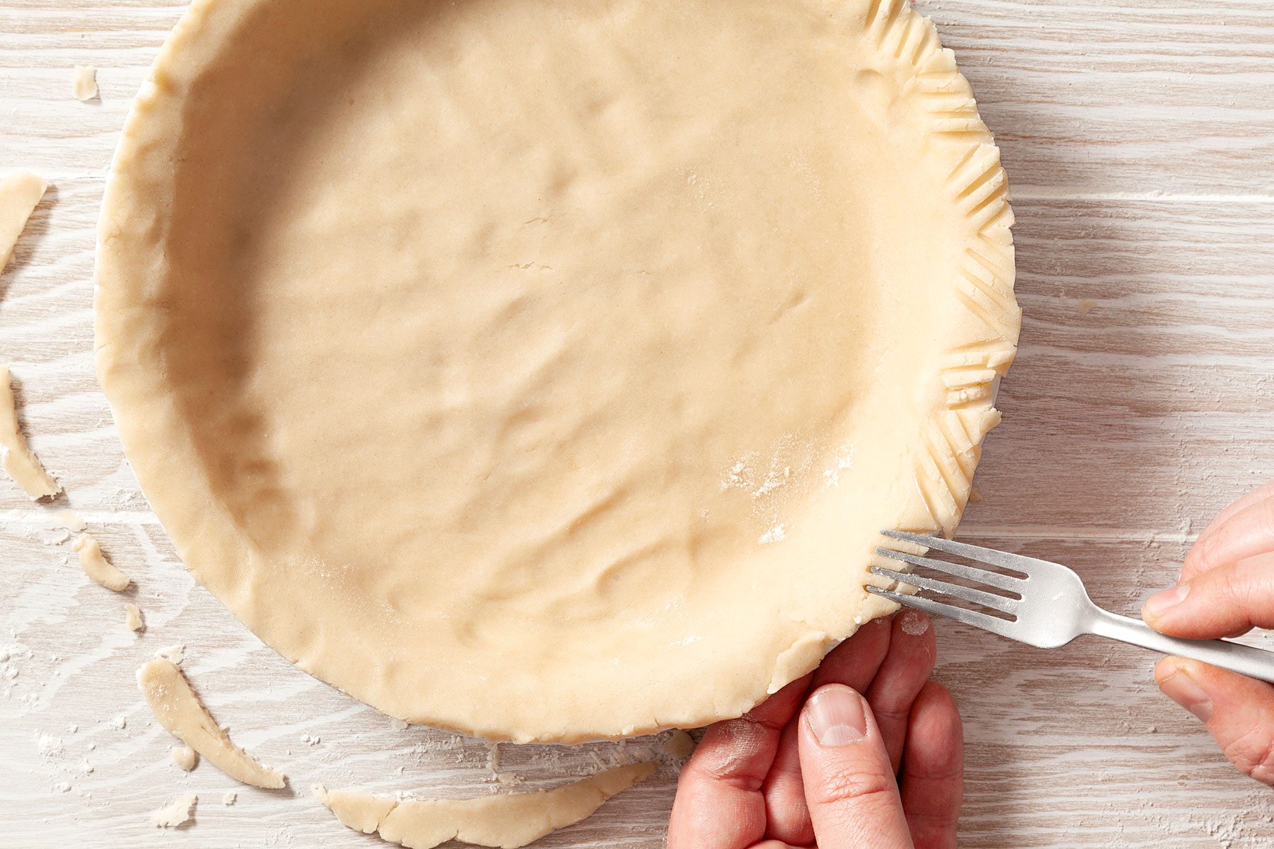 overhead shot; wooden background; Triming crust to beyond rim of plate,flute edge with fork;