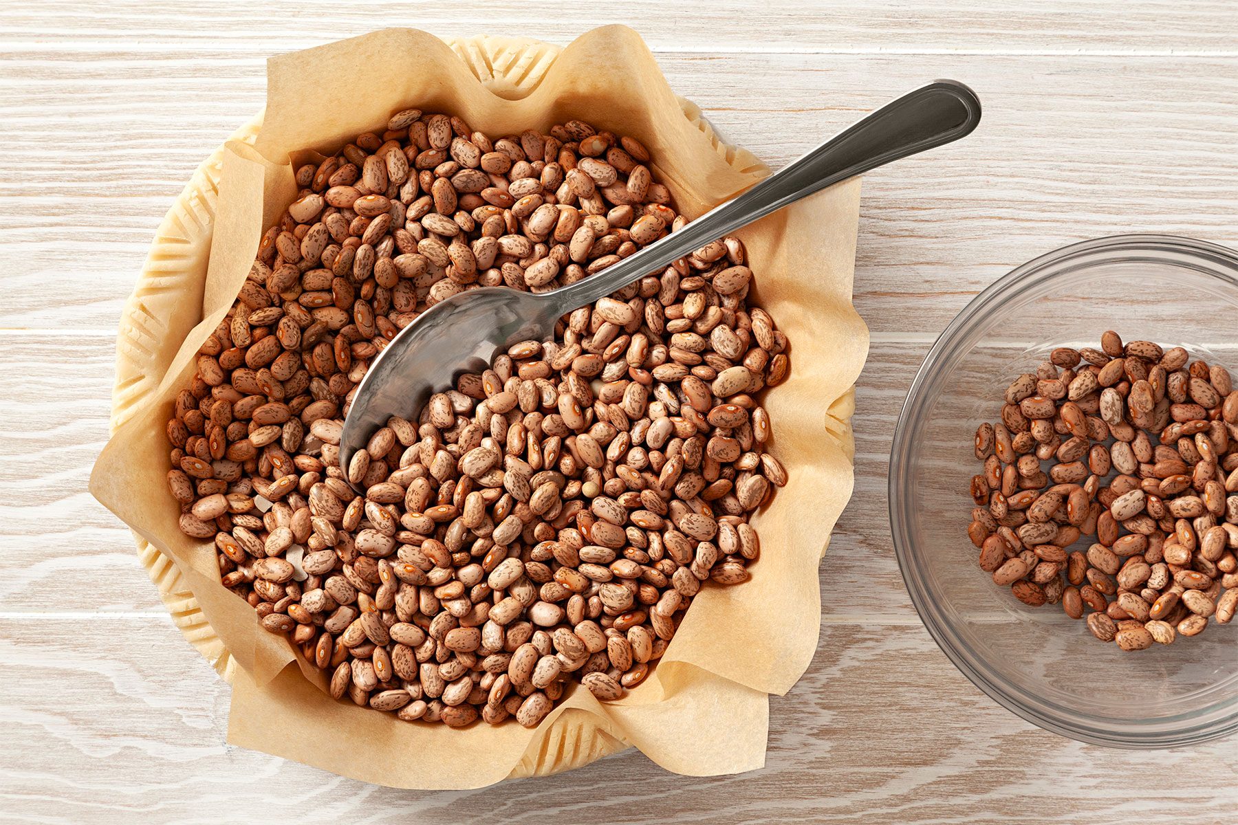 overhead shot; wooden background; Fill with pie weights, dried beans over parchment paper; one small spoon on it;