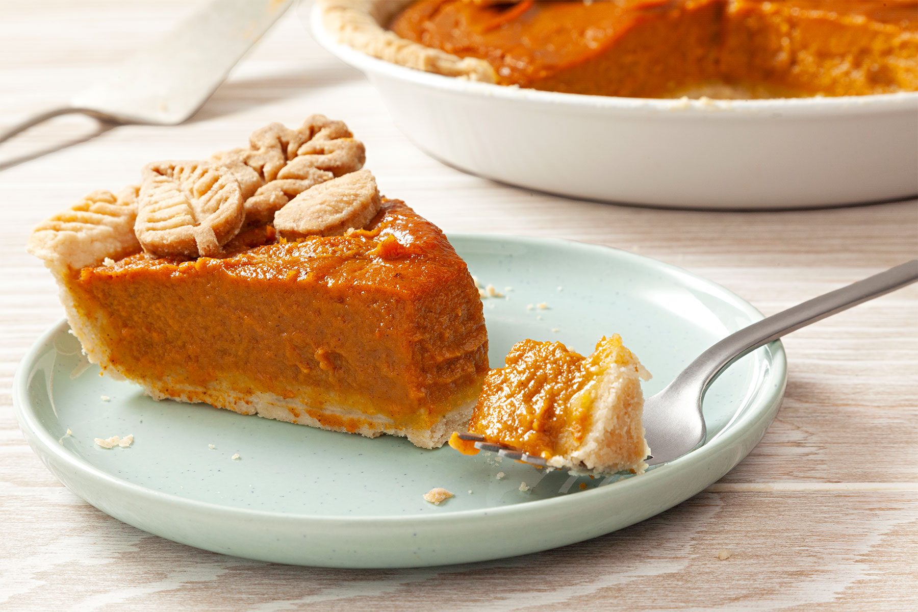 horizontal shot; wooden background; Pumpkin Pie piece served on small green plate with small spoon;