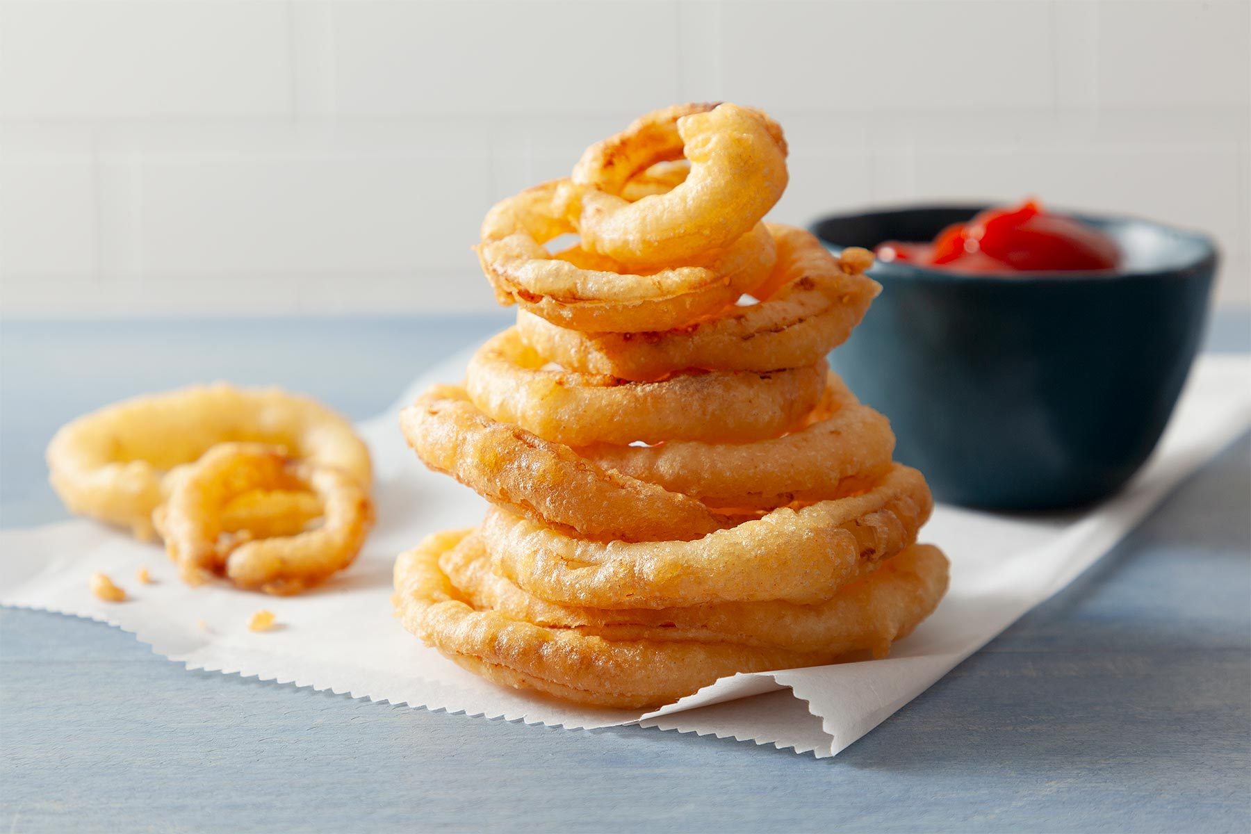 Table view shot of Crispy Fried Onion Rings; served on paper tissue with ketchup; light blue wooden background;