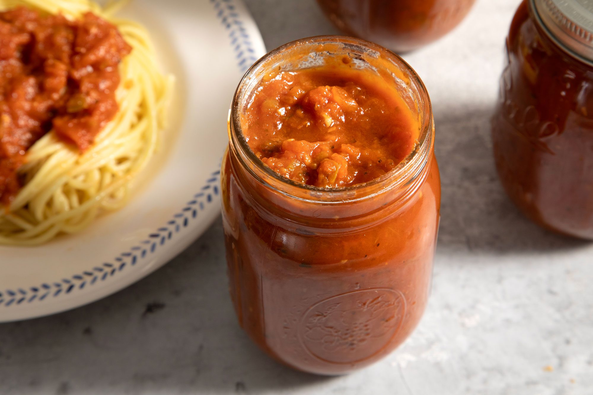 A jar of Homemade Canned Spaghetti Sauce and spread on top of spaghetti