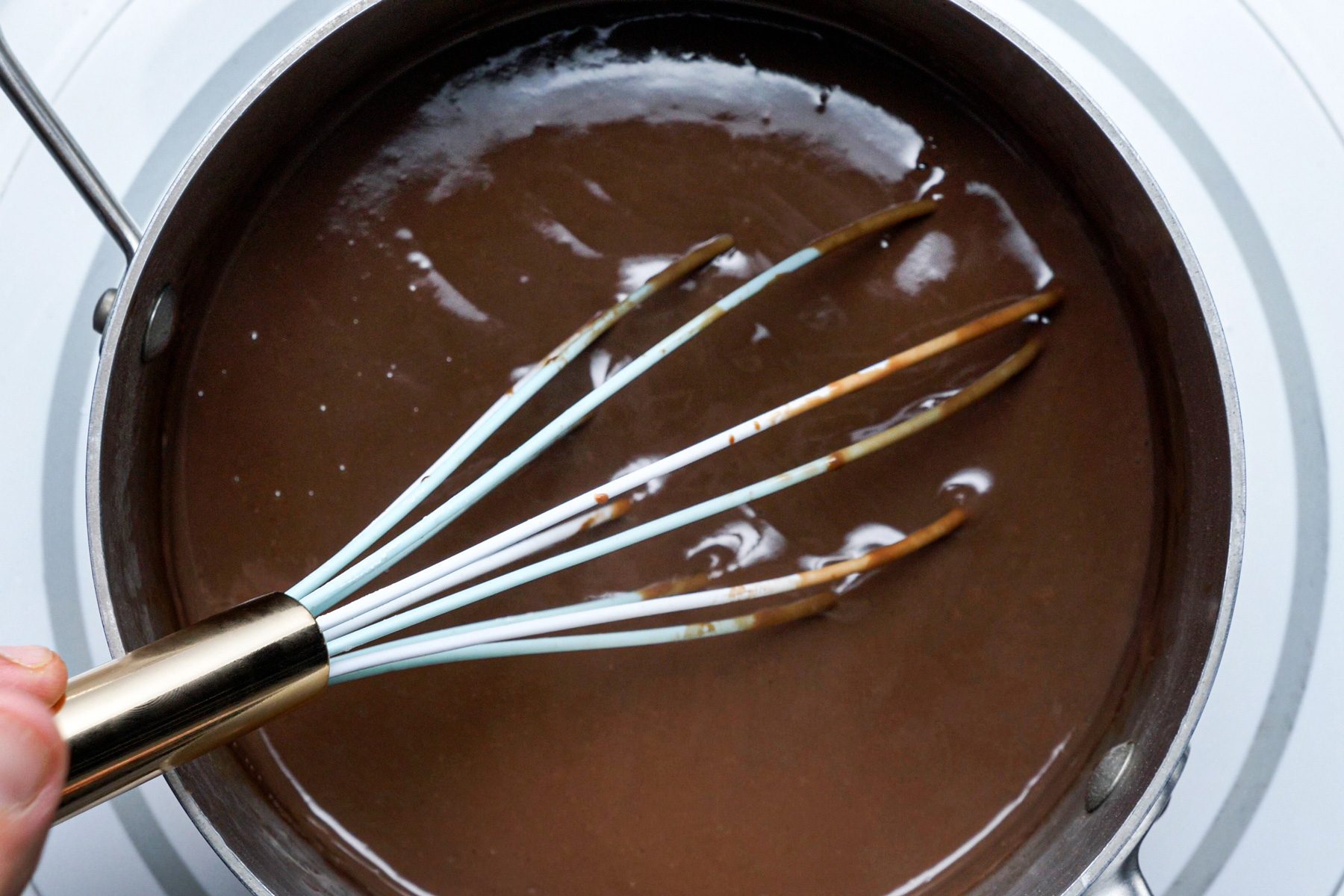 A person is stirring liquid chocolate in a pan with a whisk
