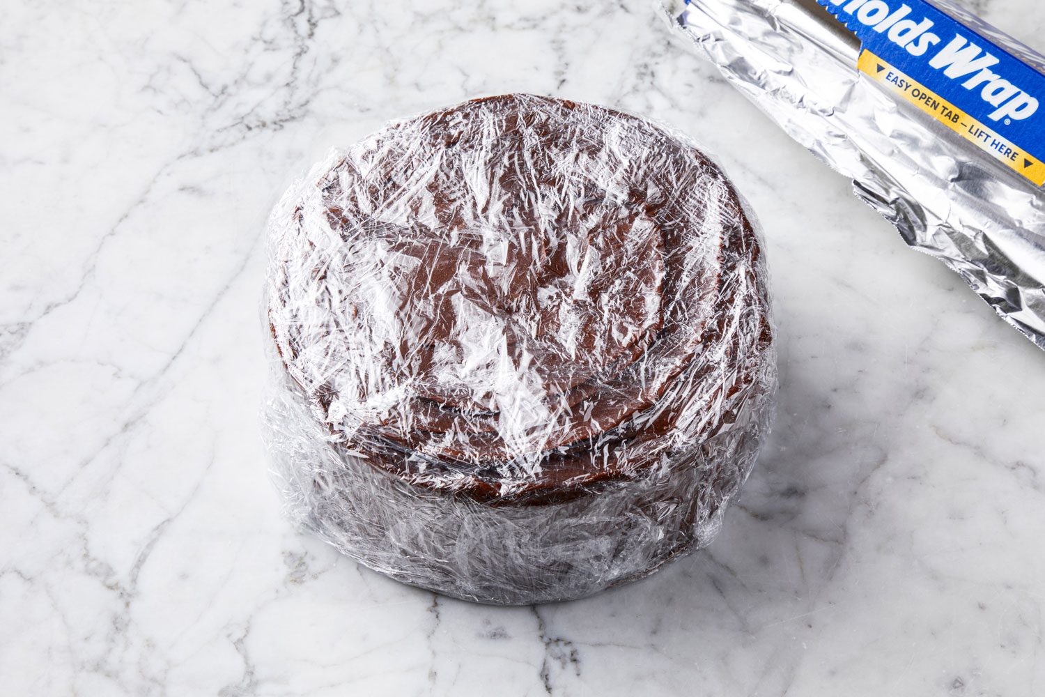 High angle view shot of a frosted Cake wrapped in two layer of plastic wrap with aluminum foil nearby on marble background