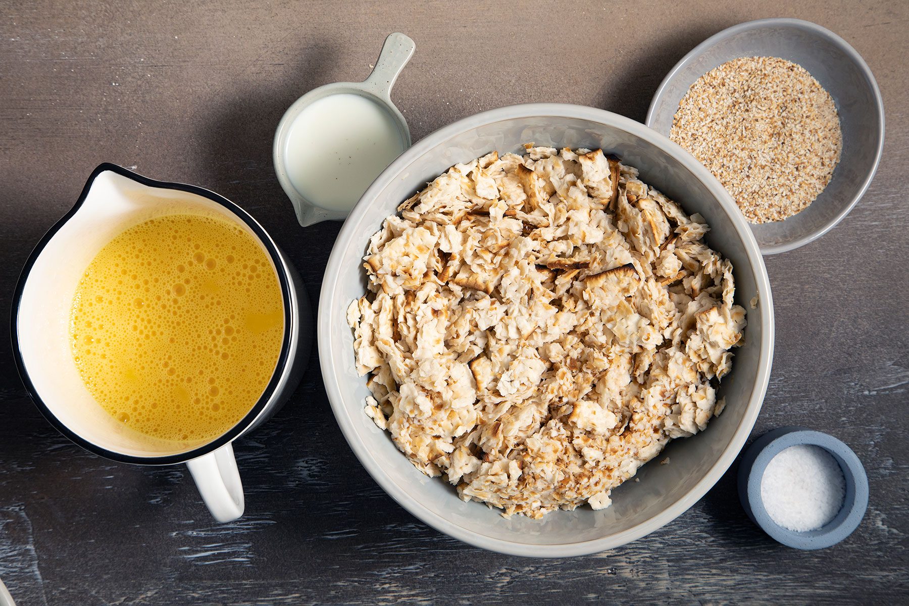 whisked eggs in a bowl, milk in a bowl, salt in a small cup and crumbs soaking in a large bowl