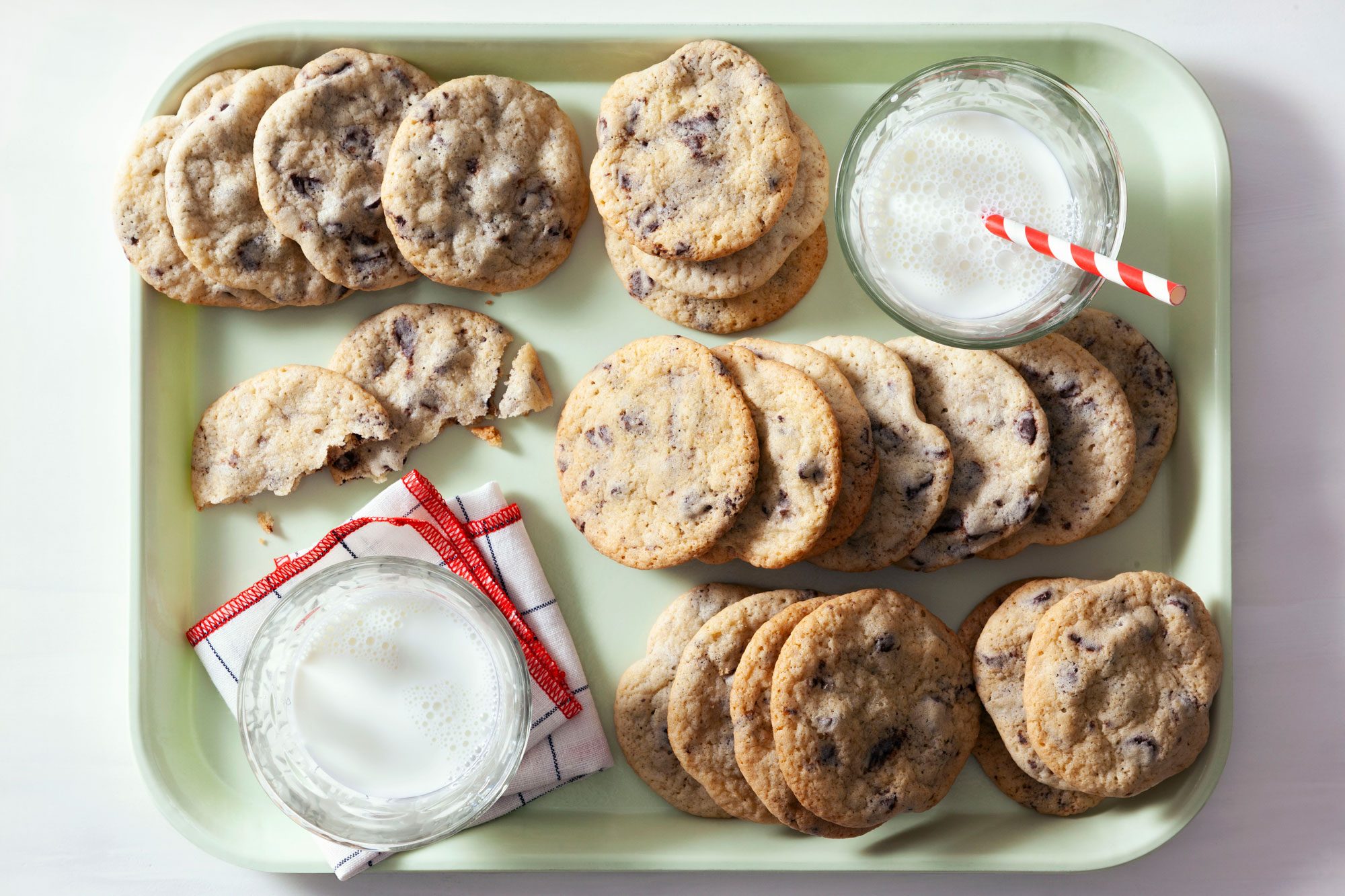 A lot of Mint Chocolate Chip Cookies with two glasses of milk placed on a light green tray.