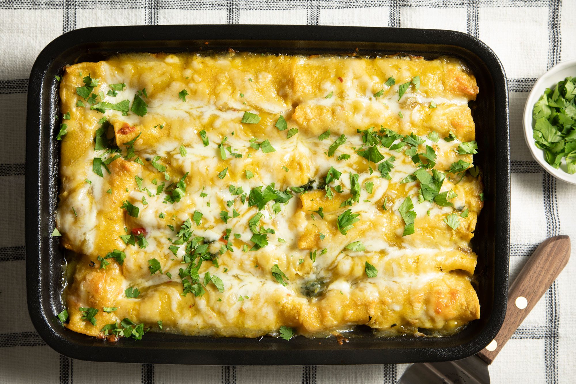 overhead shot; white background; baked Shrimp Enchiladas with Green Sauce in baking dish over kitchen towel;