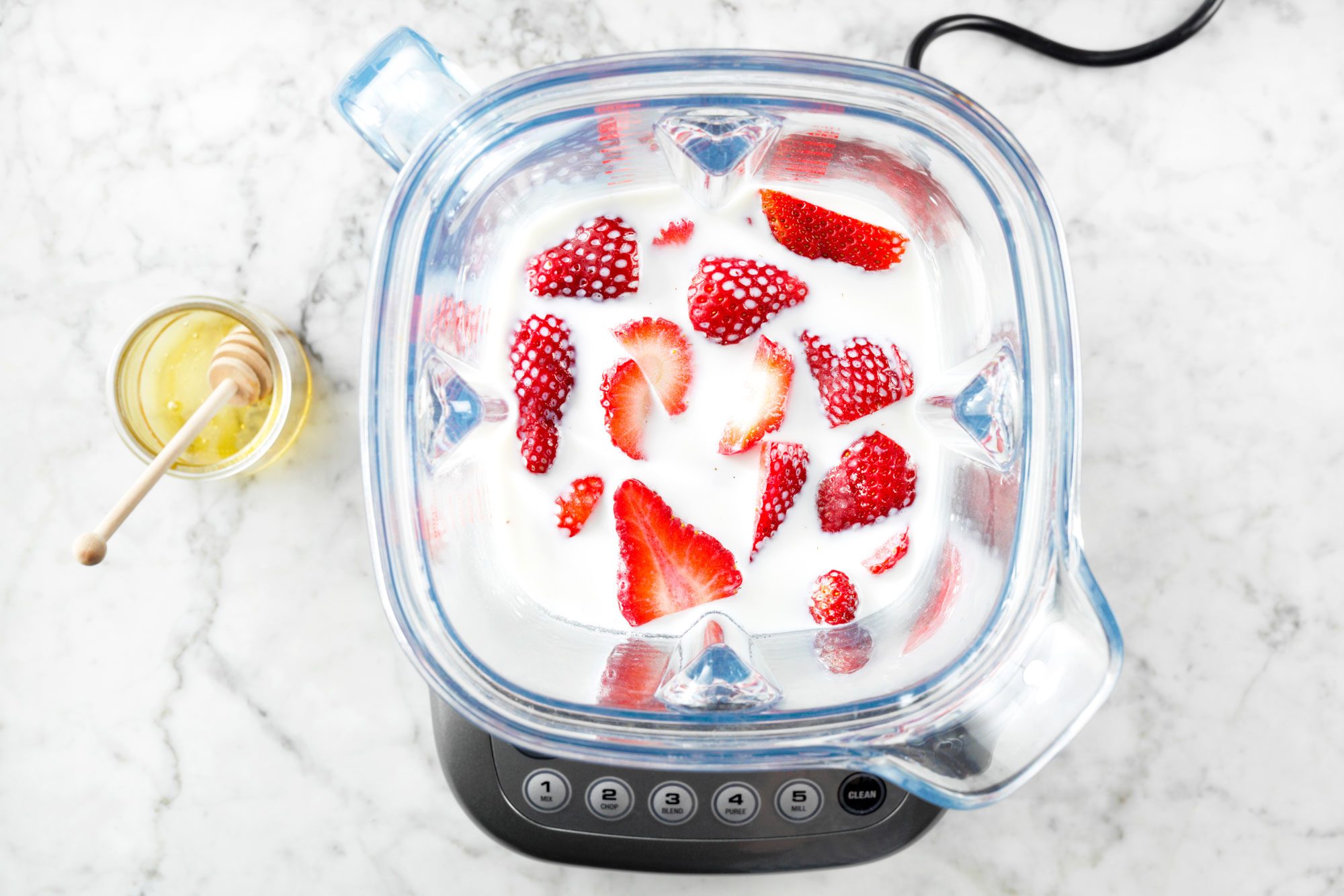 overhead shot of strawberries in a blender with milk on marble surface