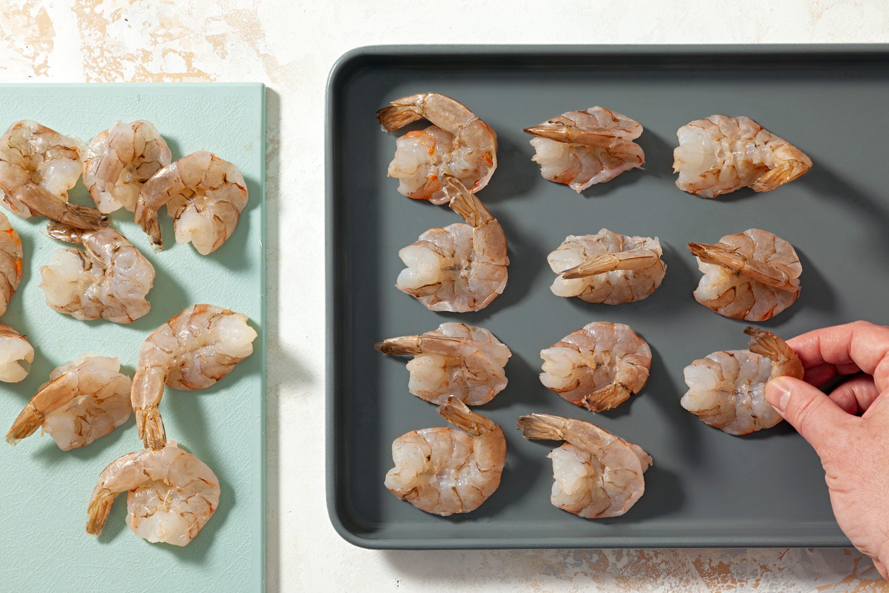 A person placing shrimp on a baking pan