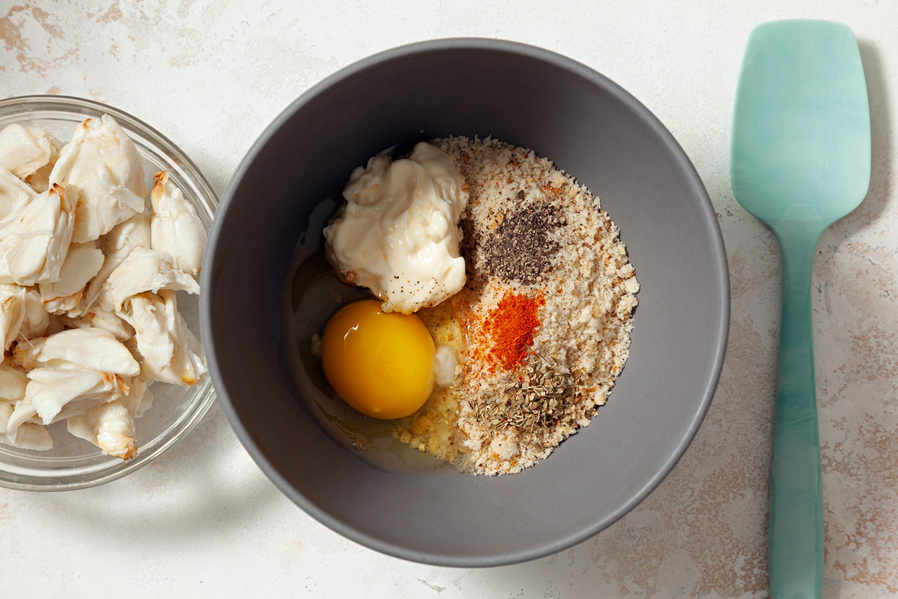 A bowl of ingredients and a bowl of crab, along with a spatula.