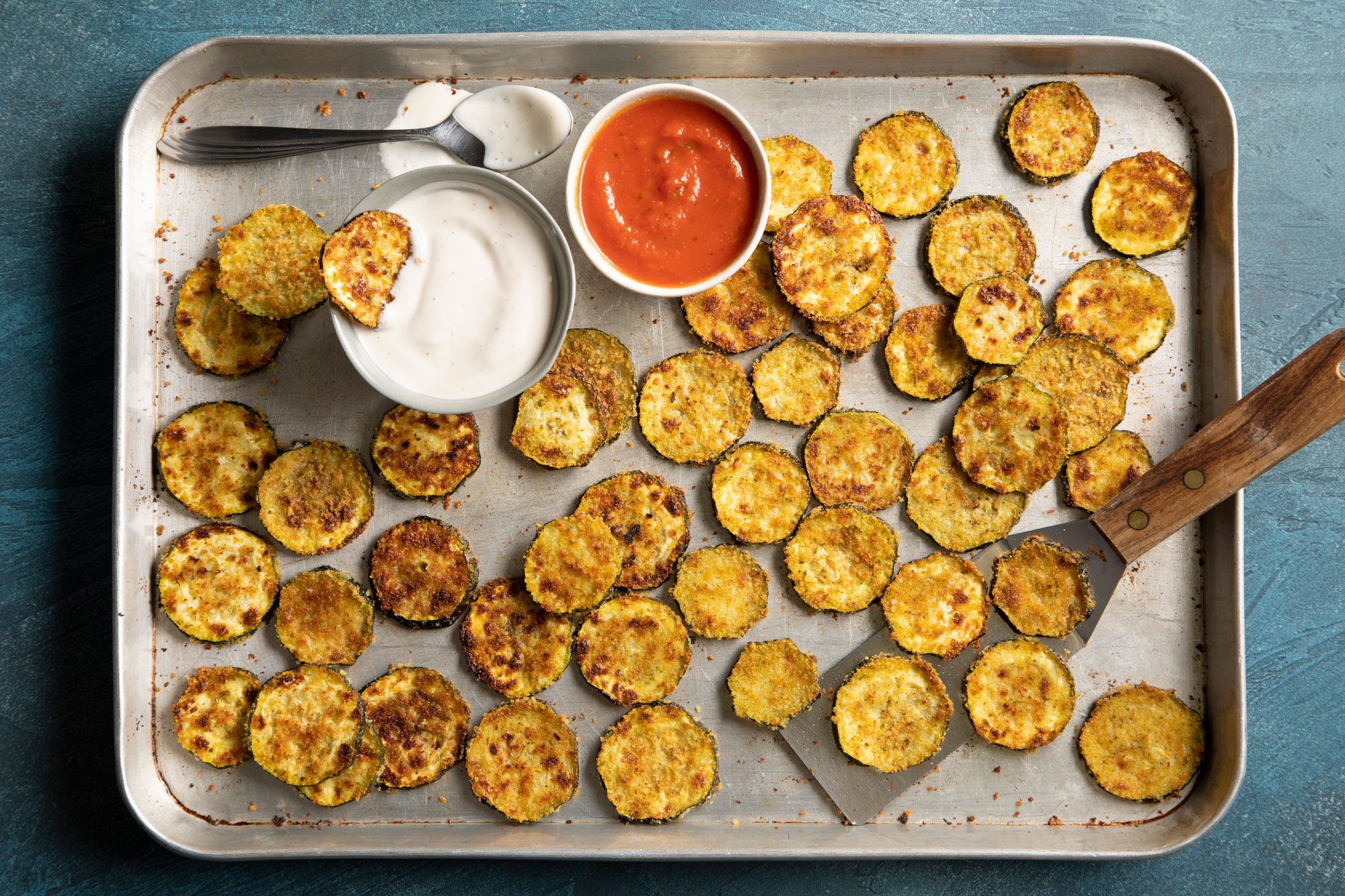 Tray of zucchini chips with a side of dipping sauce and parmesan cheese