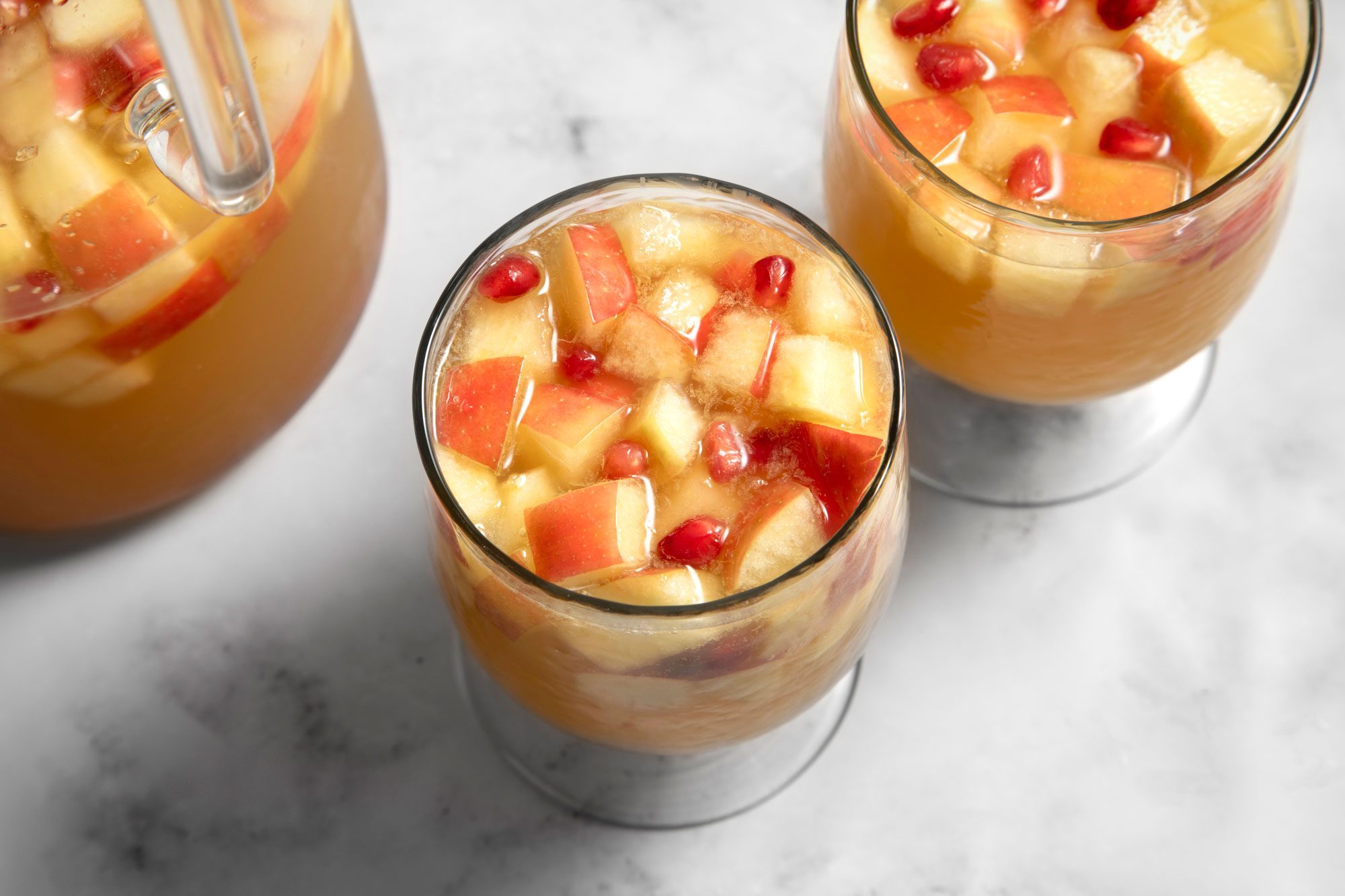 Overhead shot of Apple Cider Sangria; in a large pitcher; served in two glasses; marble background;