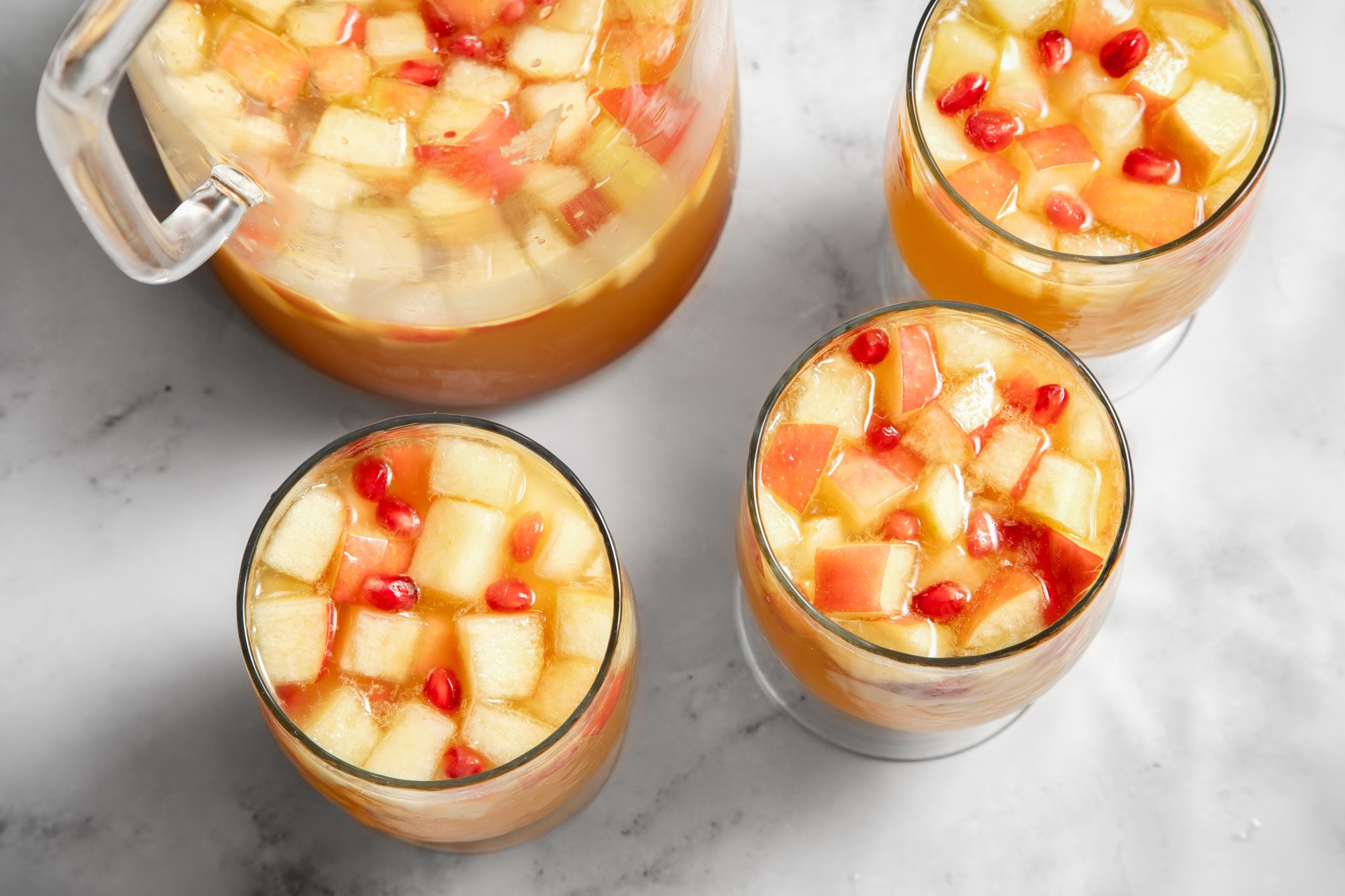 Top view shot of Apple Cider Sangria; in a large pitcher; served in glasses; marble background;