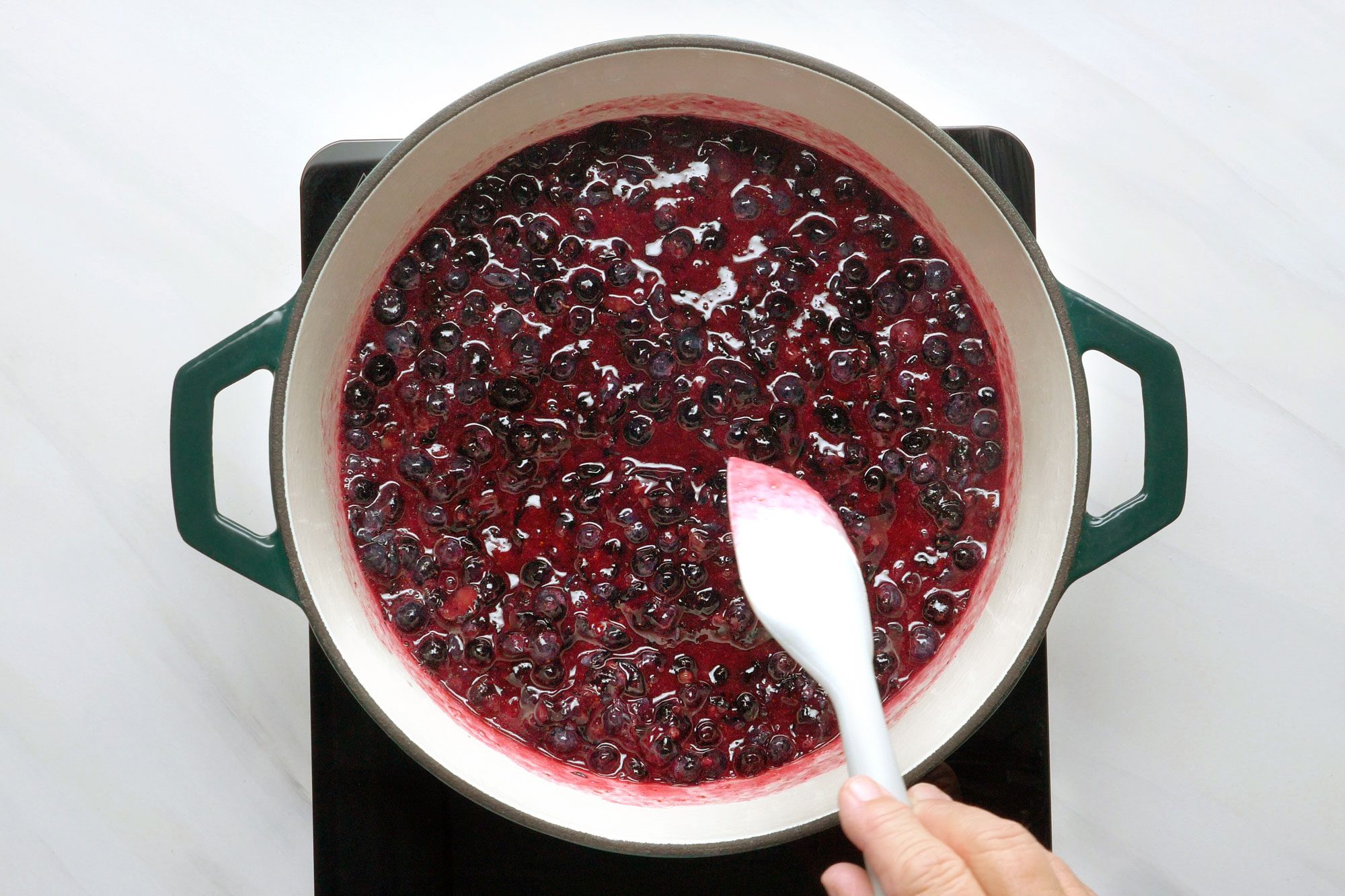 overhead shot of stirring blueberries in a dutch oven