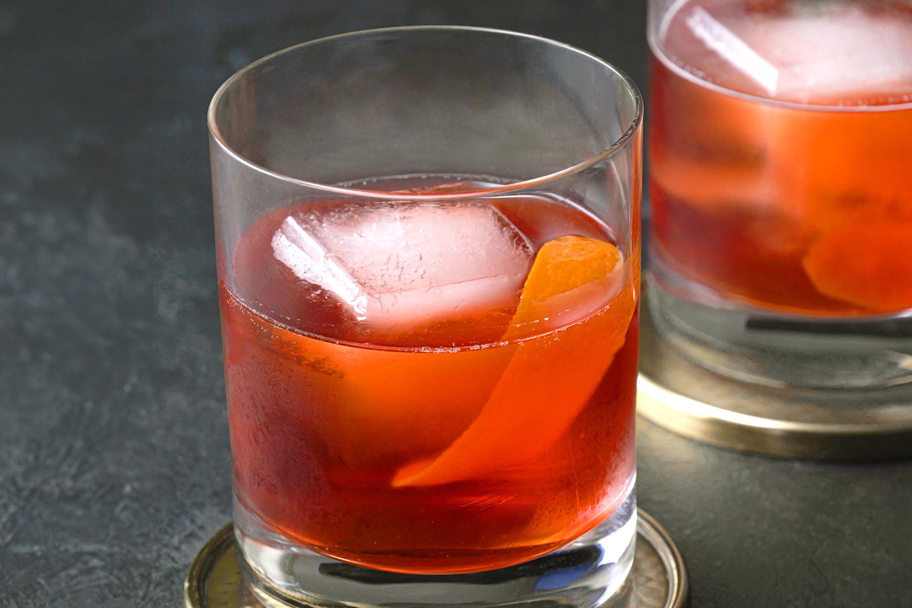 A glass of Boulevardier cocktail garnished with orange peel on golden coaster plates