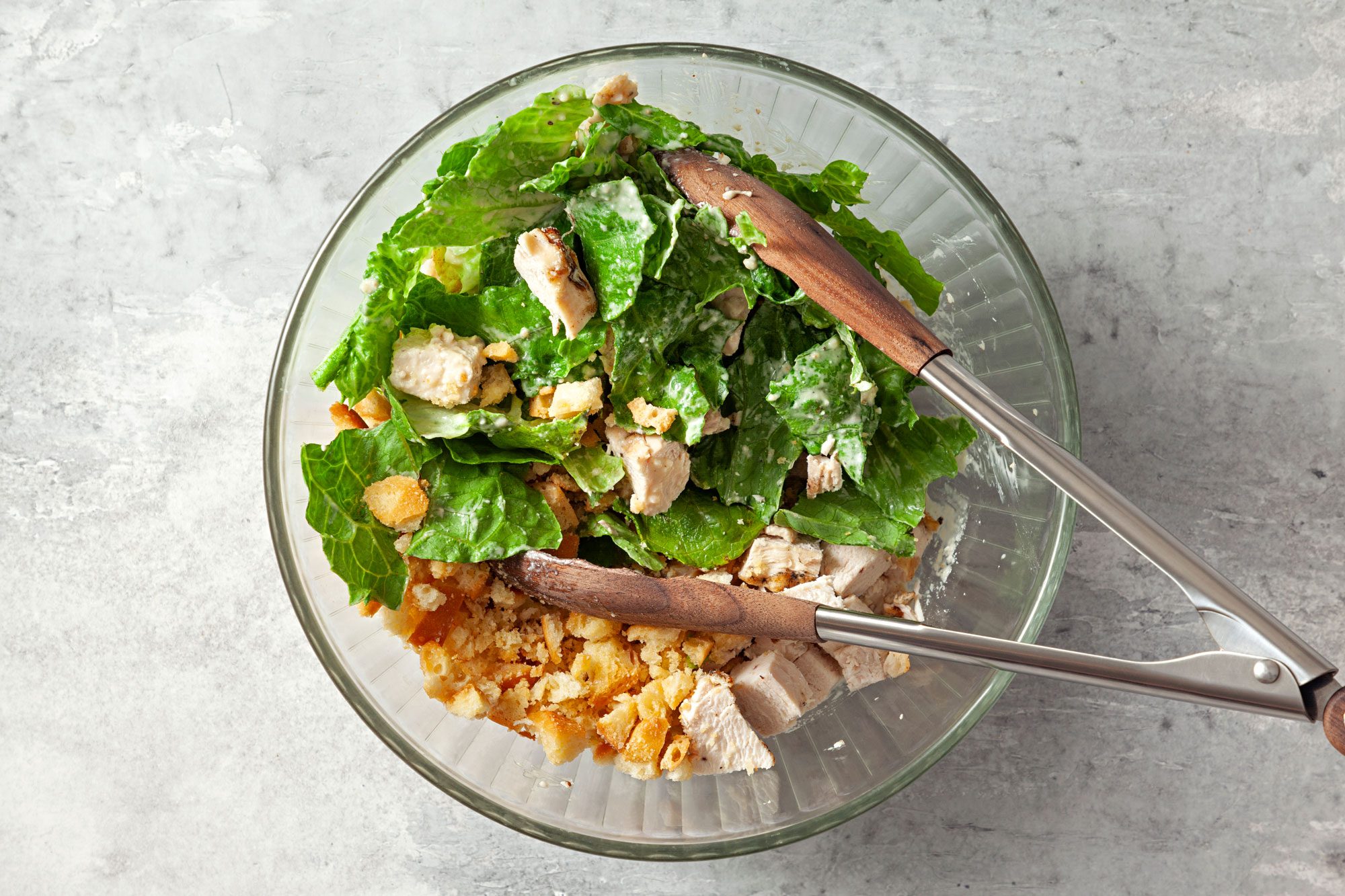 overhead shot of chicken, croutons and romaine added in the dressing in a large bowl