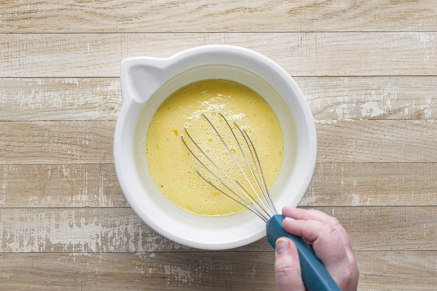 A person is Mixing Beated egg in a bowl using hand mixer