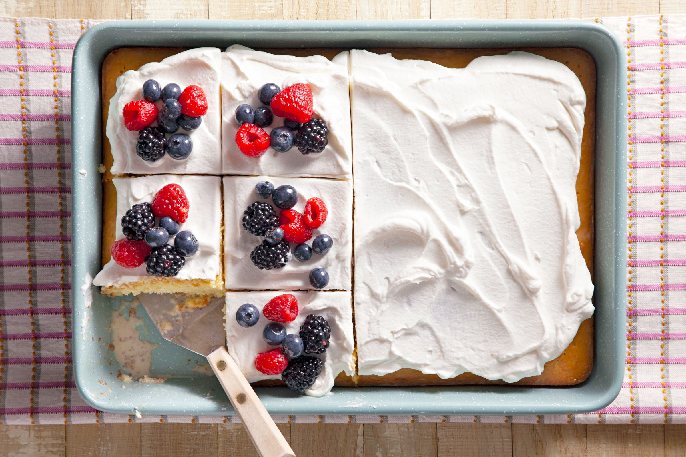Easy Tres Leches Cake slices in a pan and half are topped with berries