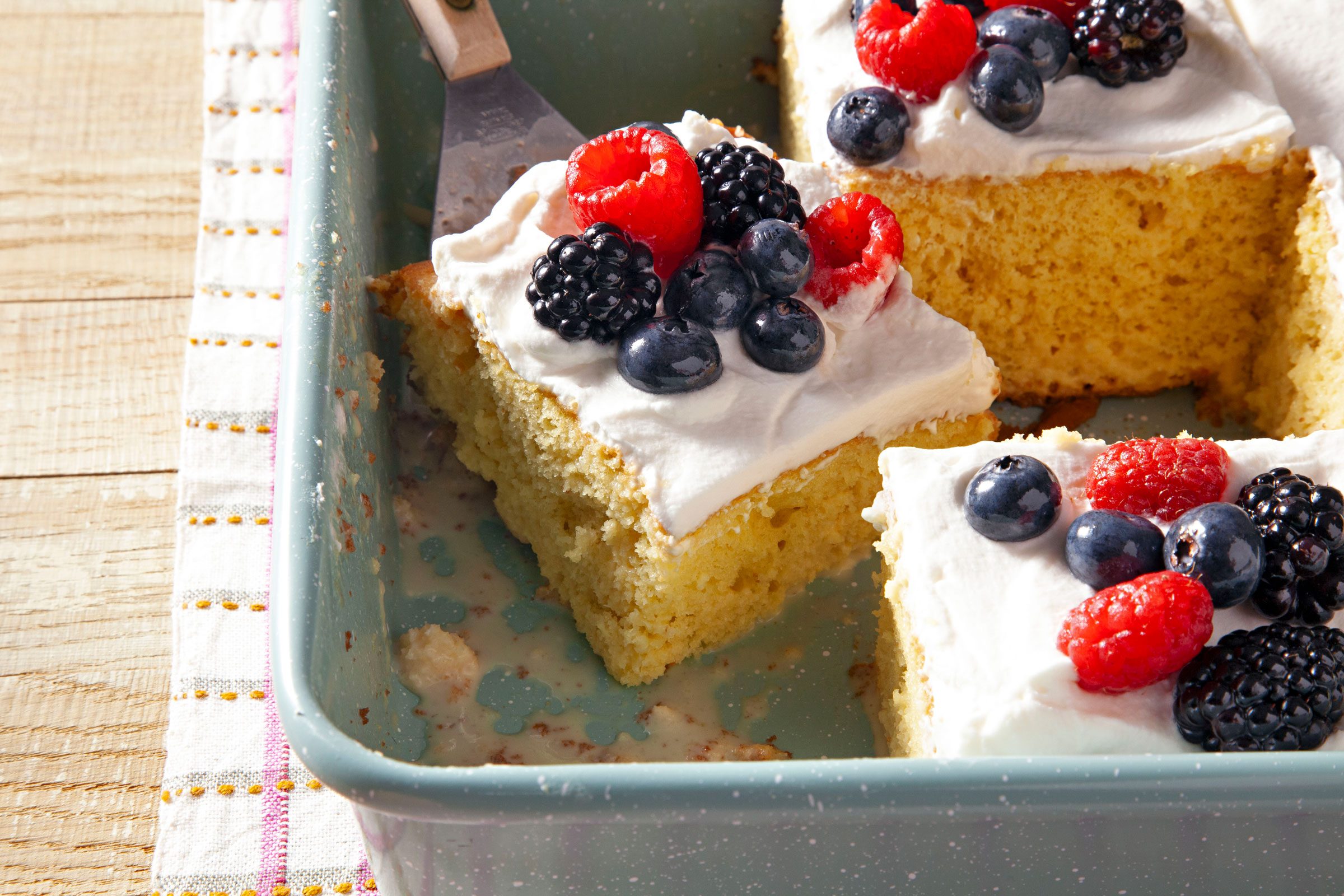 Easy Tres Leches Cake slices in a pan topped with berries