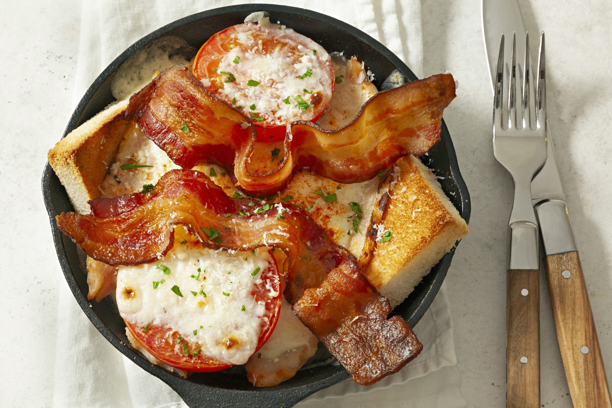 A black pan of Kentucky Hot Brown with a sliver knife and a fork on a table