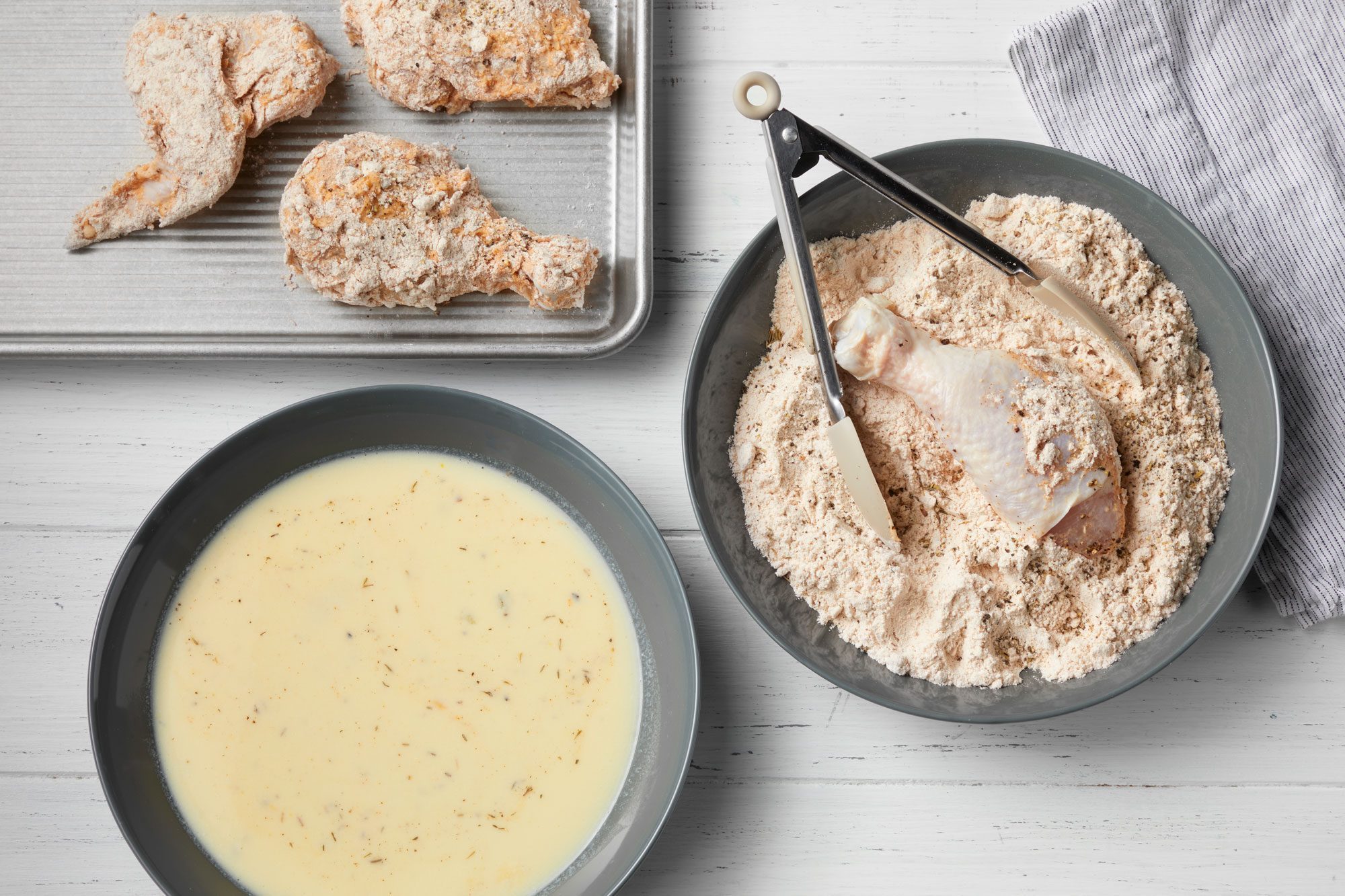 overhead shot of dipping and coating chicken to fry; tong; bowls; wooden background;