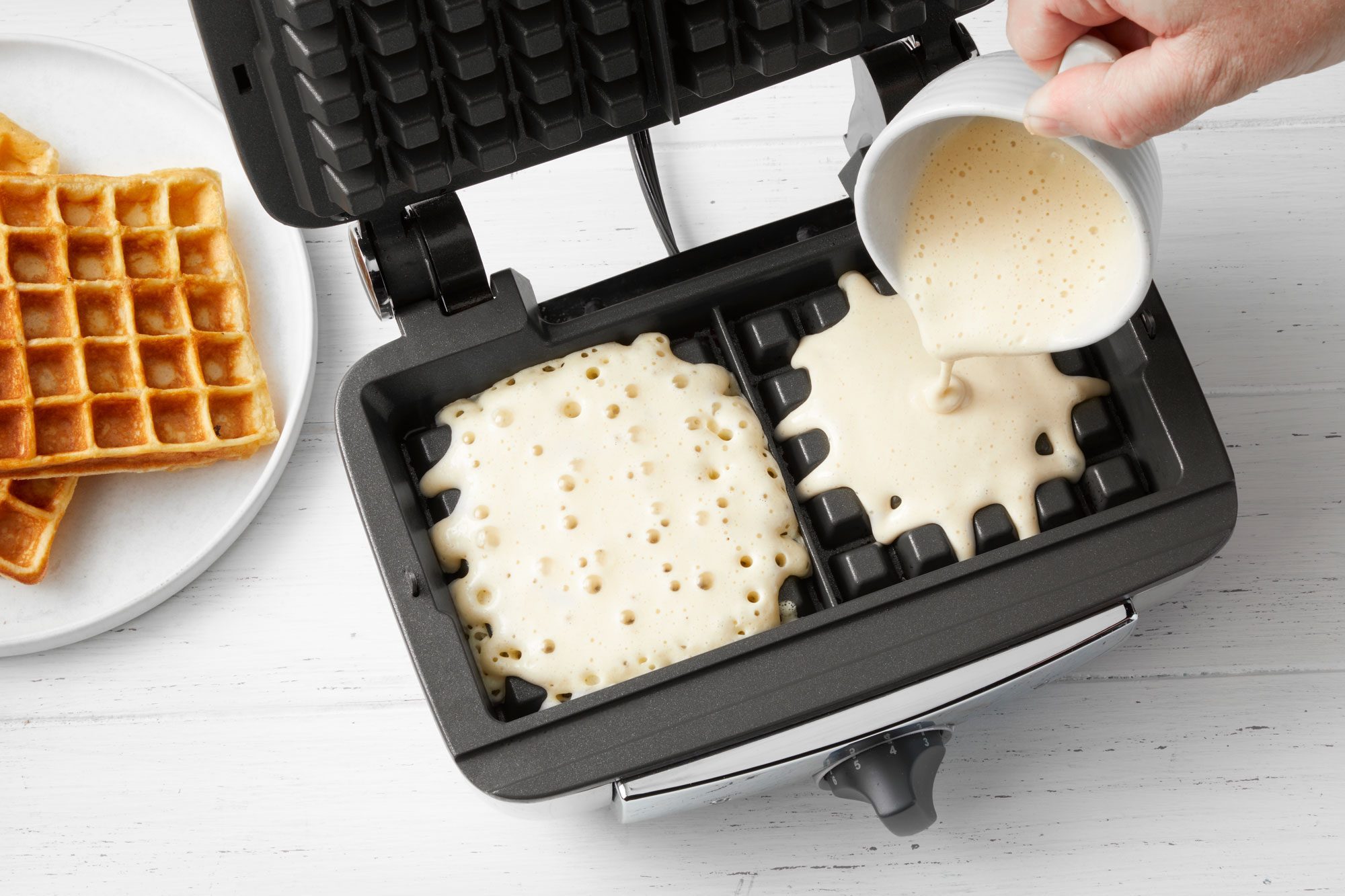 overhead shot of pouring waffle batter in a waffle maker; wooden background;