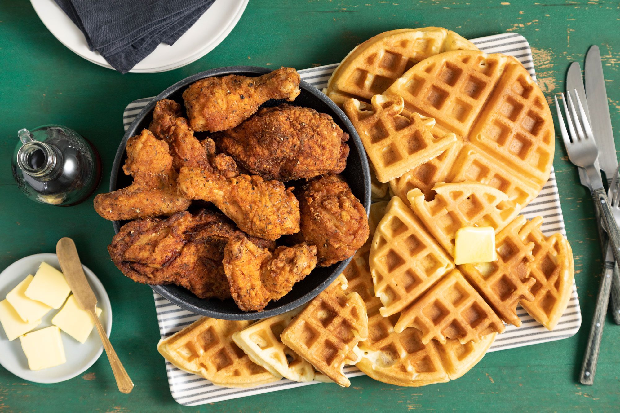 overhead shot of Fried Chicken And Waffles served on a tray; butter cubes; green background;