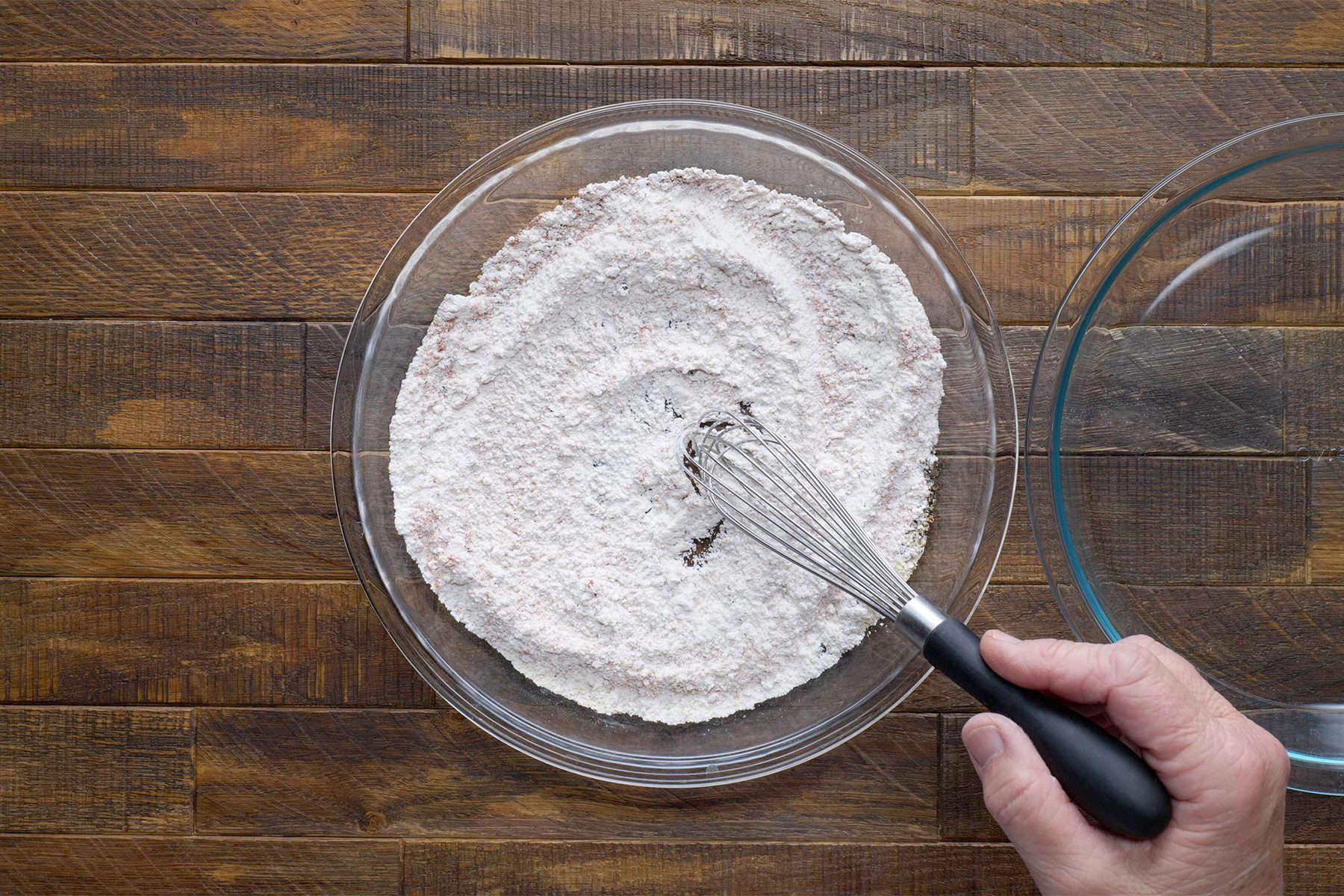 a person mixing flour and seasonings with whisk tool on wooden table