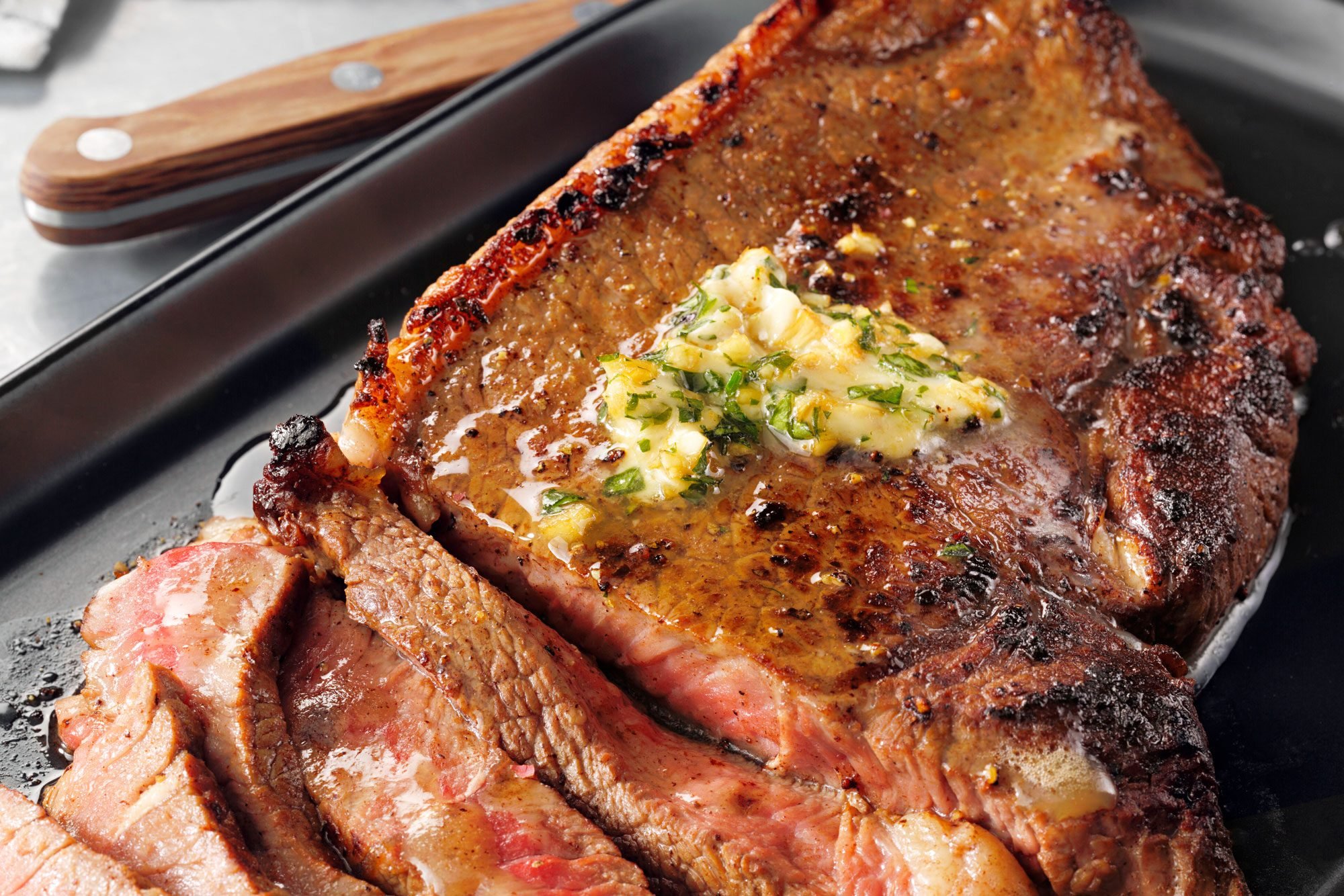 Close up of garlic-butter steak placed on a black serving plate, garnished with butter