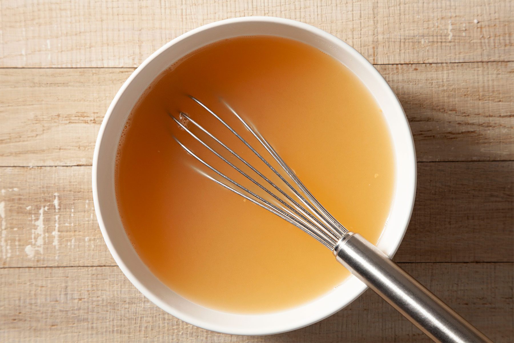 Overhead shot of combine water and ham base; stir until combined; whisk tool; wooden background;