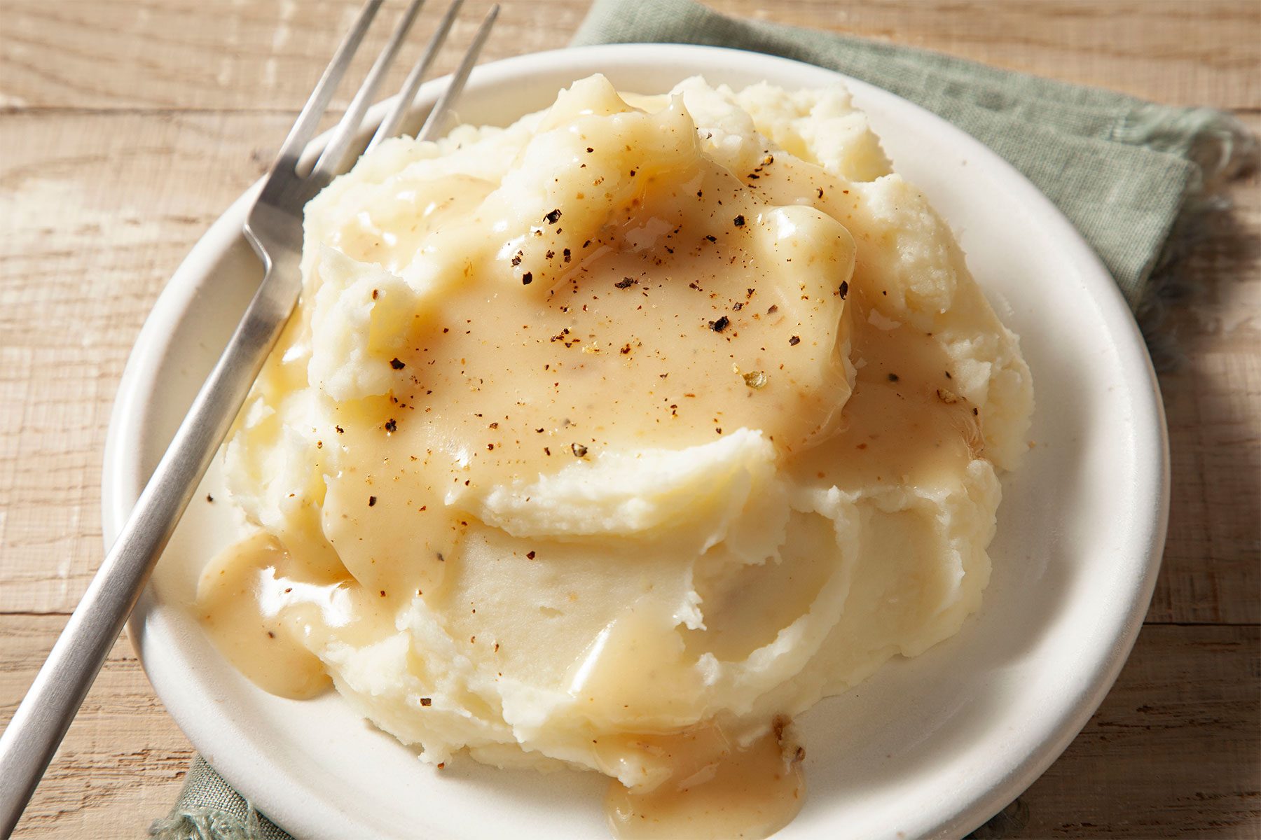 High angle view shot of Ham Gravy; poured over ham mashed potatoes; on a small plate; with fork; napkin; wooden background;